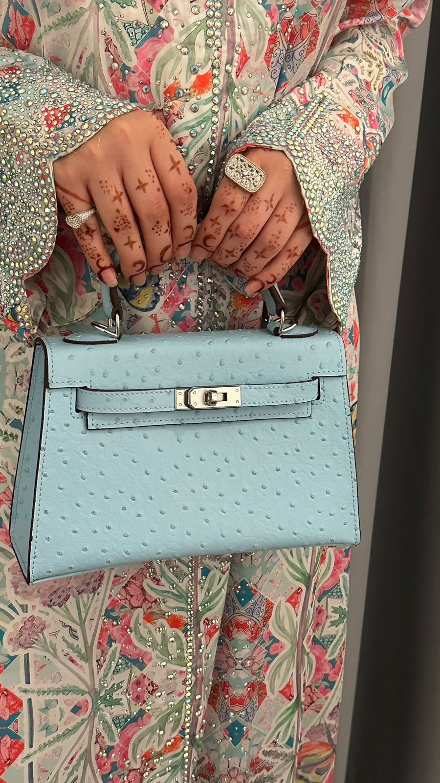 Light blue handbag held by a person wearing a patterned outfit.