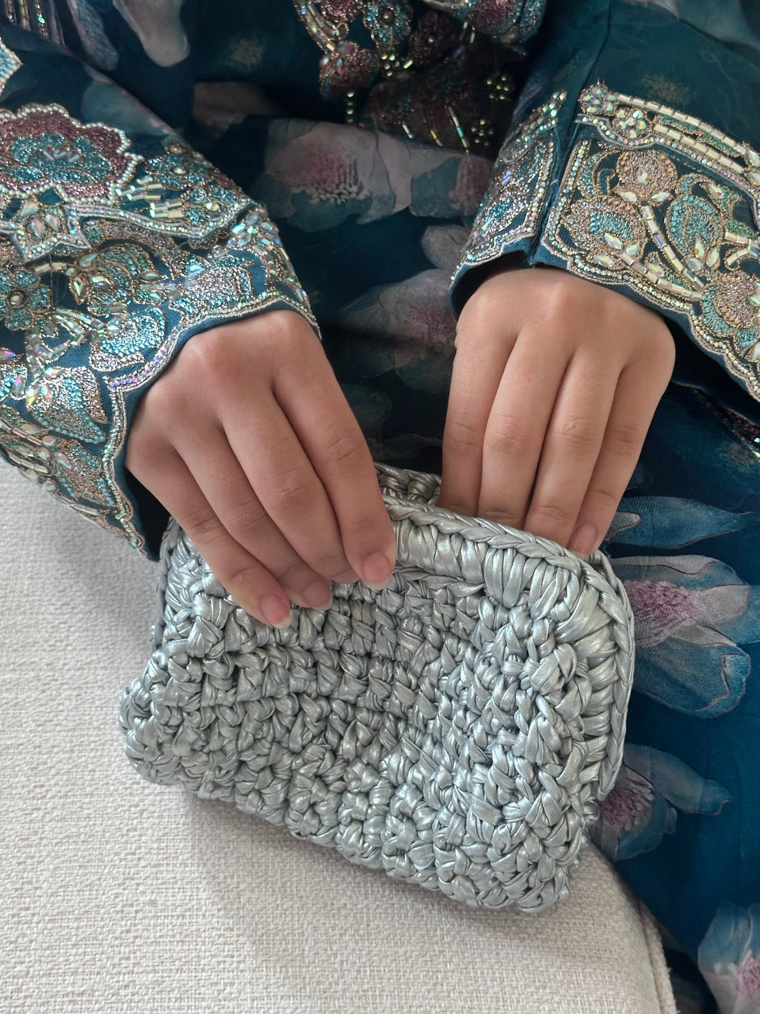 Silver textured clutch held by hands with embroidered sleeves on a light background