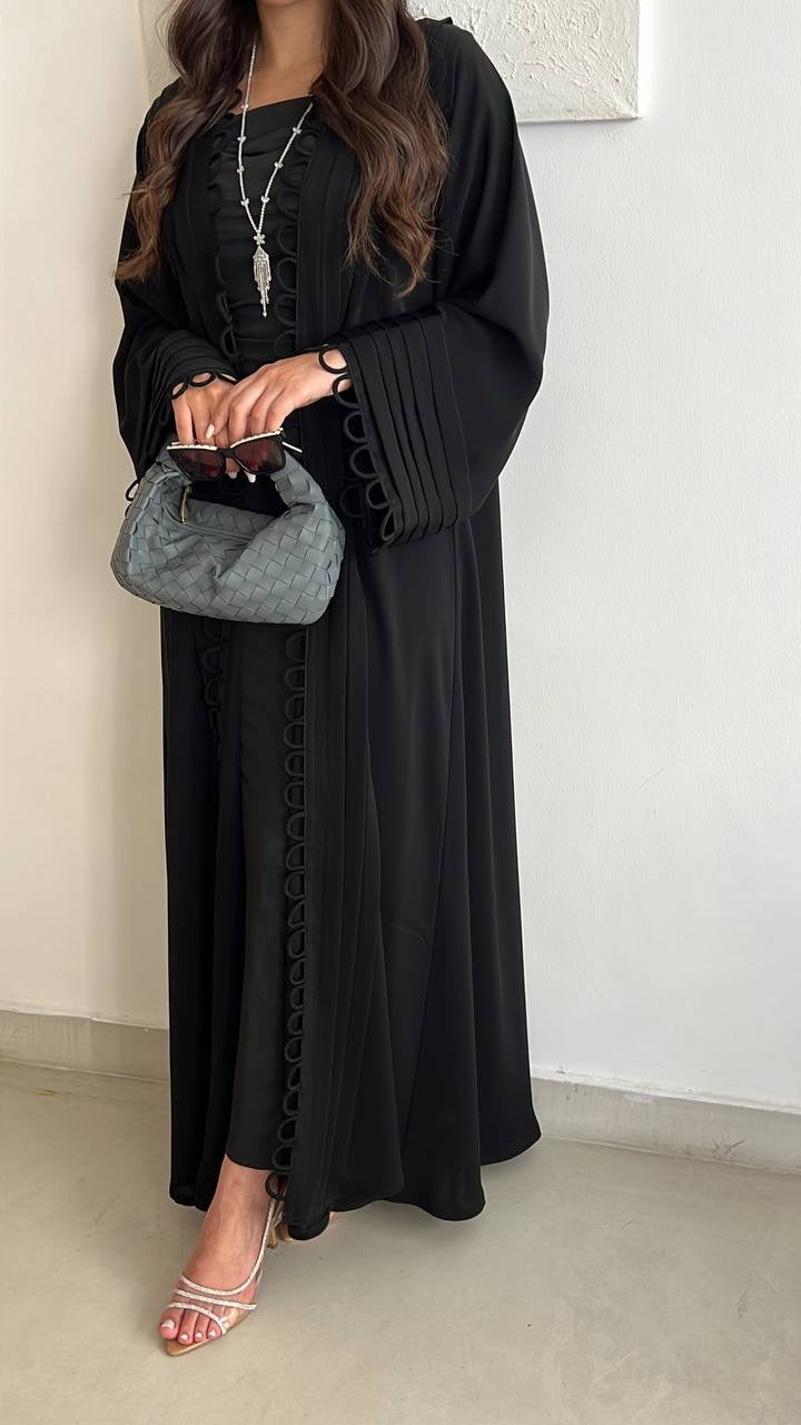 A person standing, holding a grey leather shoulder bag and wearing a black dress.