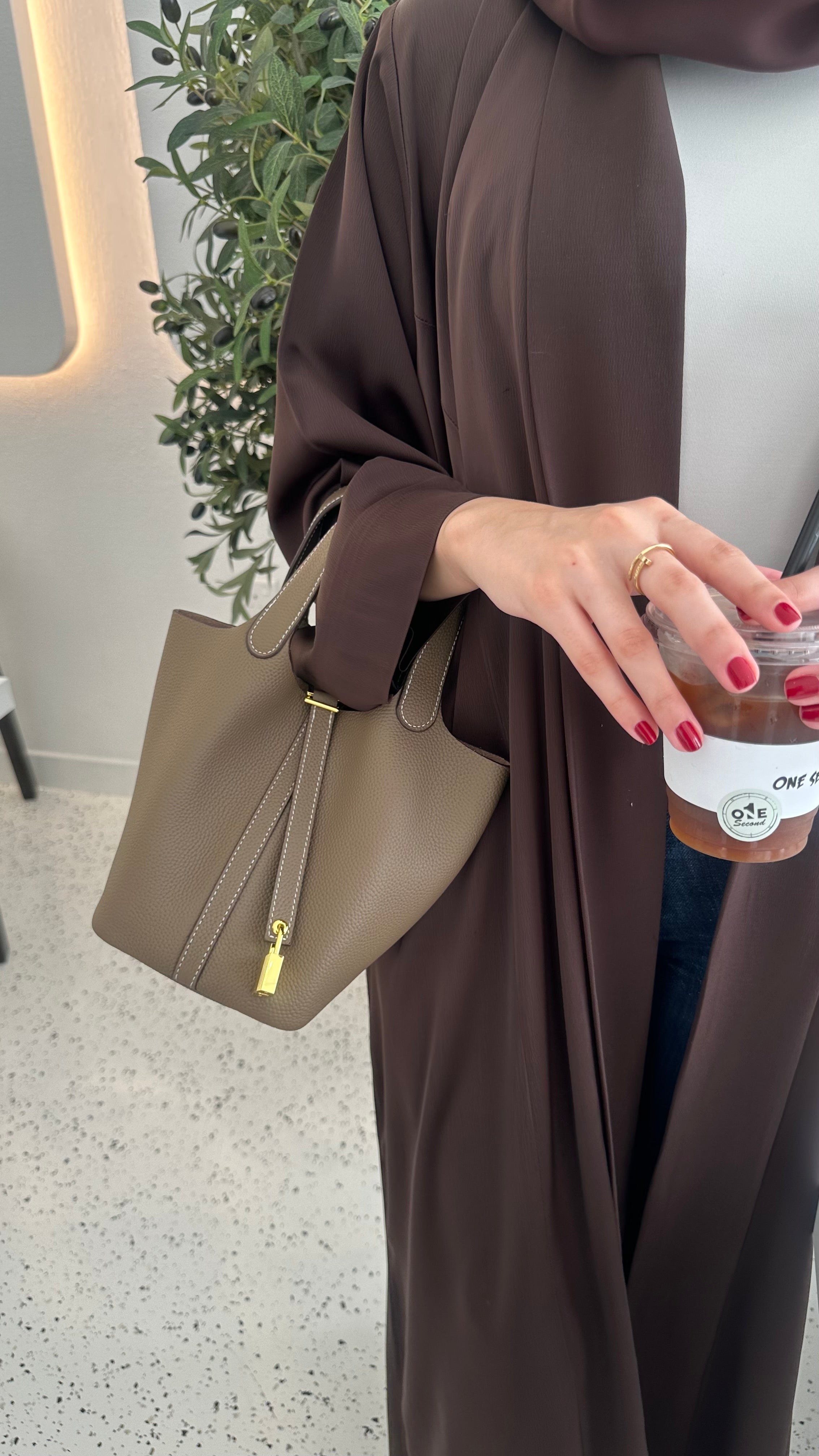 A person holding a brown leather handbag with an adjustable tab padlock in gold finish.