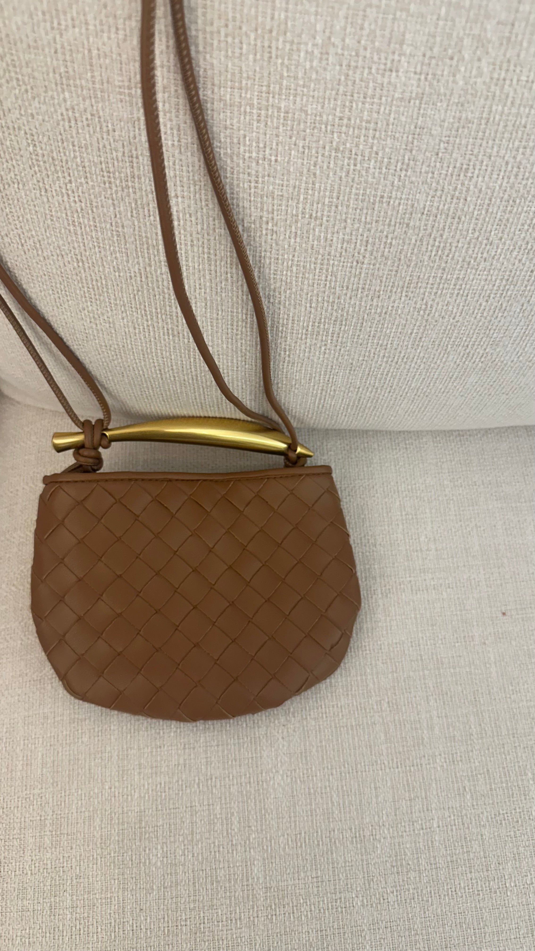 A brown mini-bag with a quilted design, featuring a strap and a metallic bar.