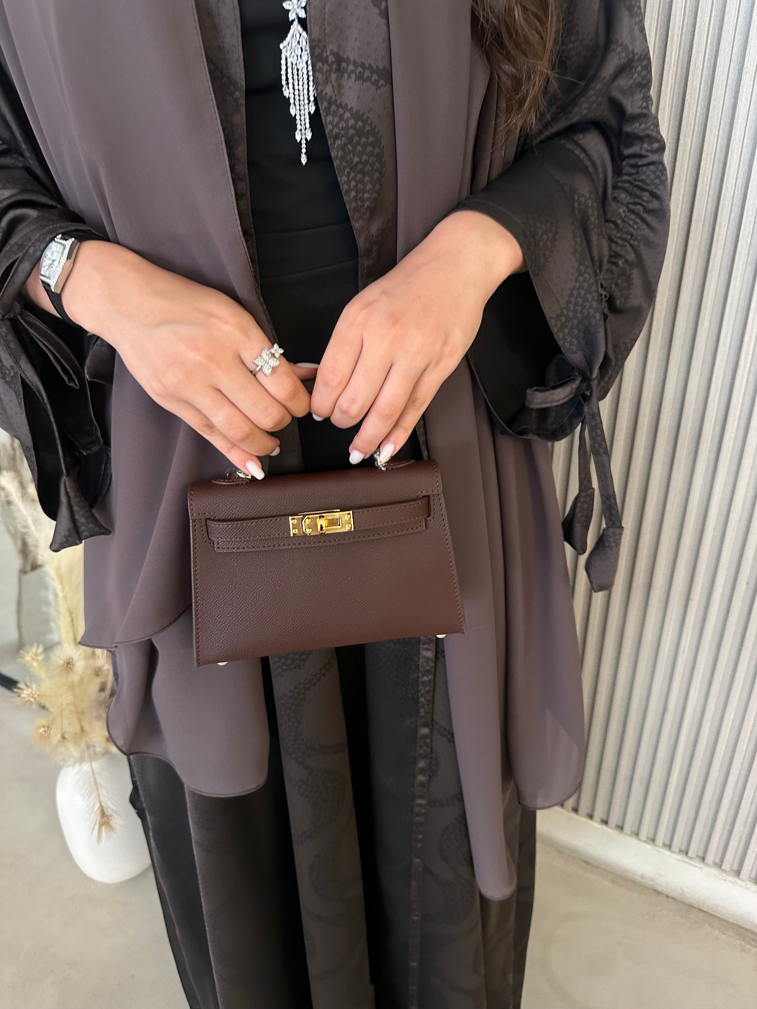 A person holding a burgundy clutch purse with a long strap.