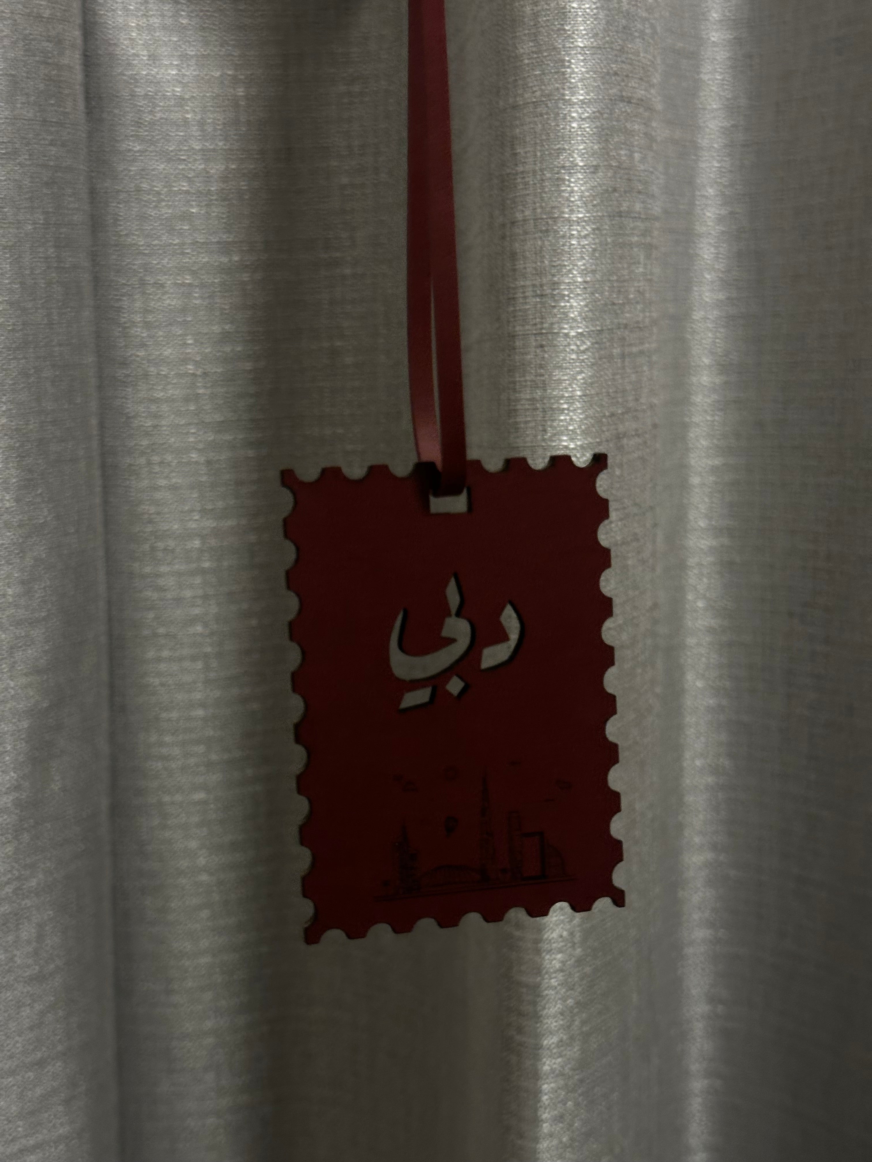 Red decorative tag with Arabic text on a gray curtain background