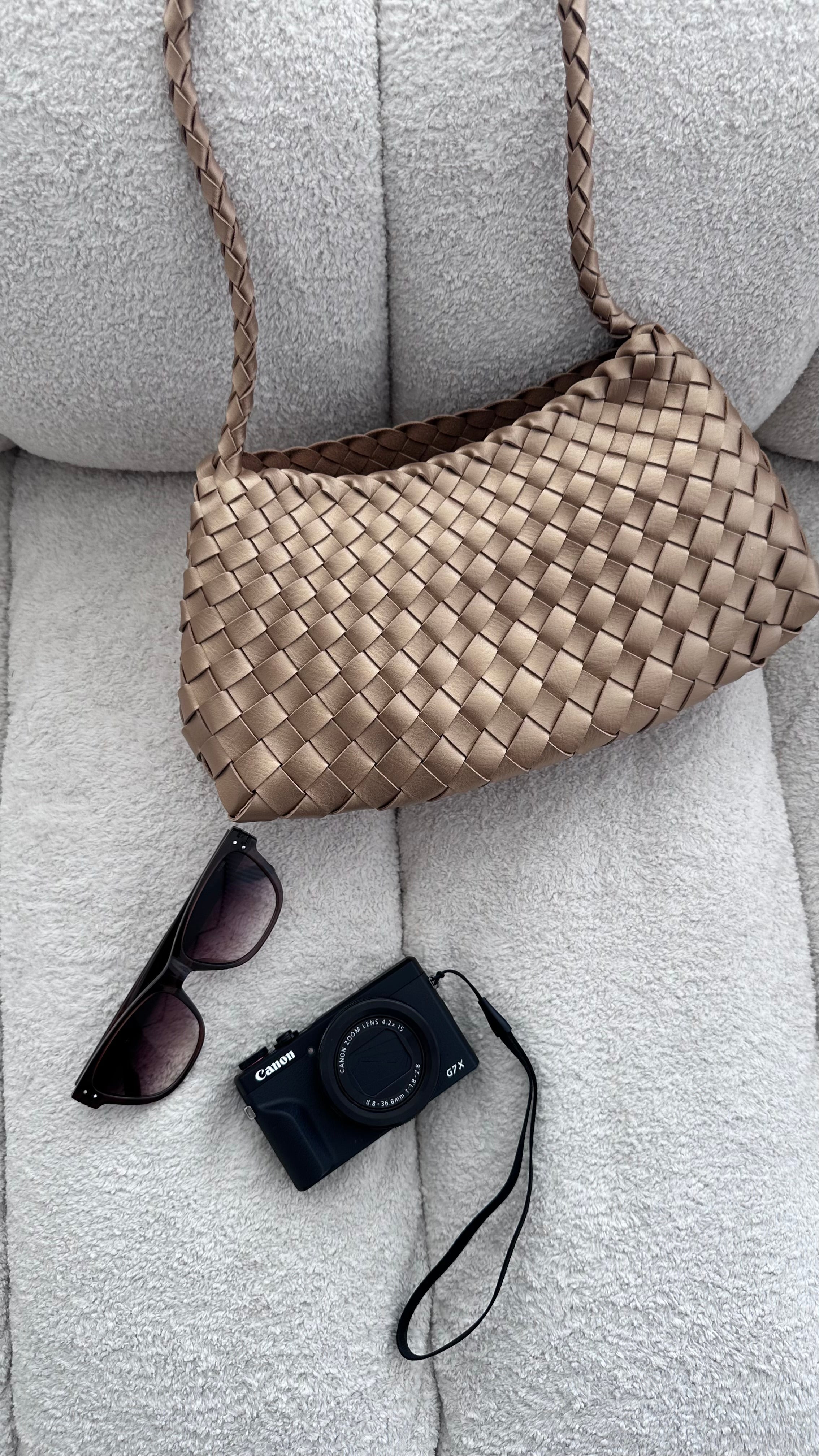 Woven handbag, sunglasses, and camera on a textured surface