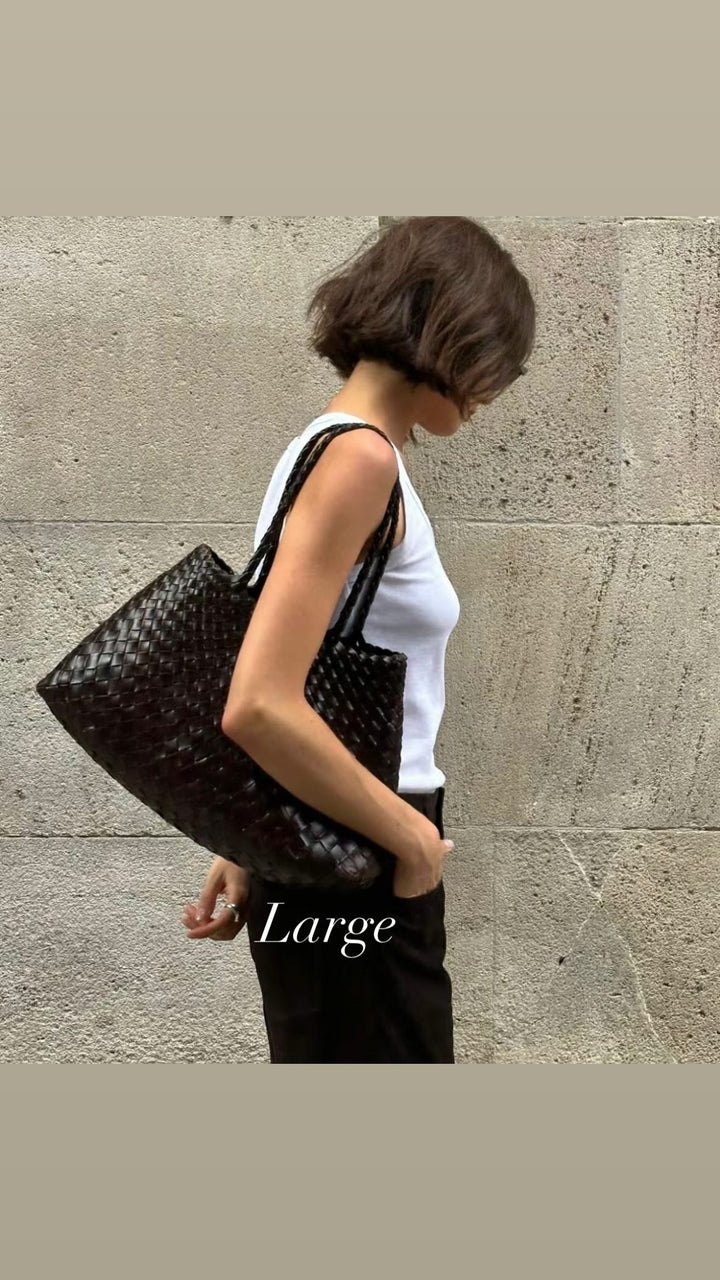 Person holding a large black woven handbag against a stone wall.