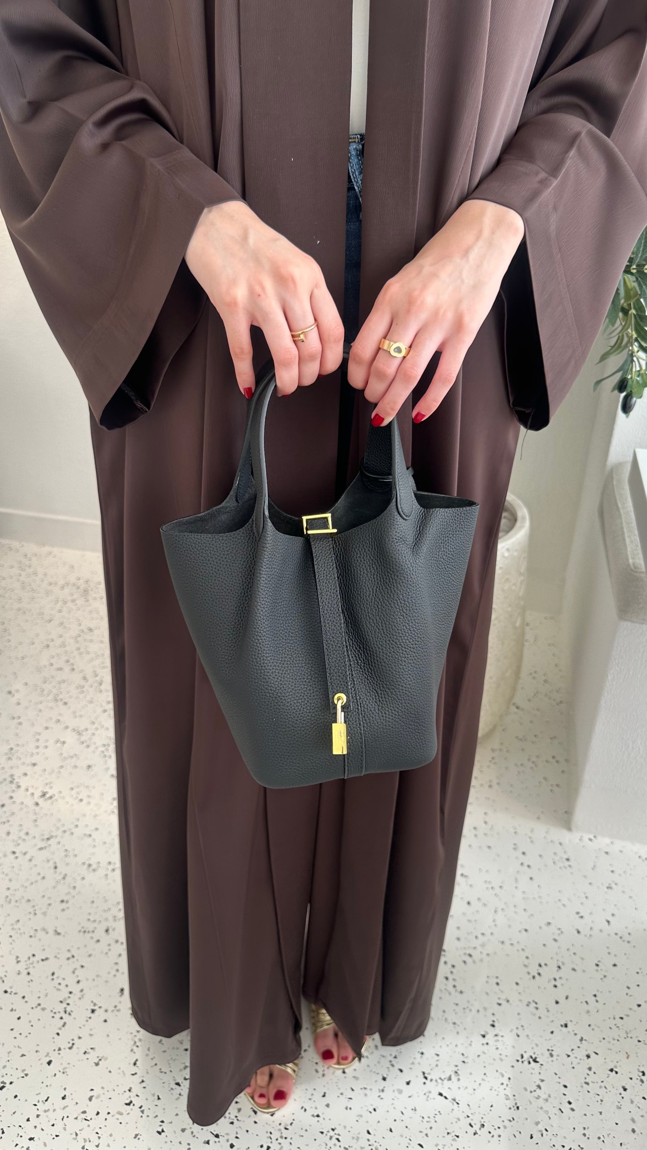 A person holding a black handbag with a gold finish padlock.