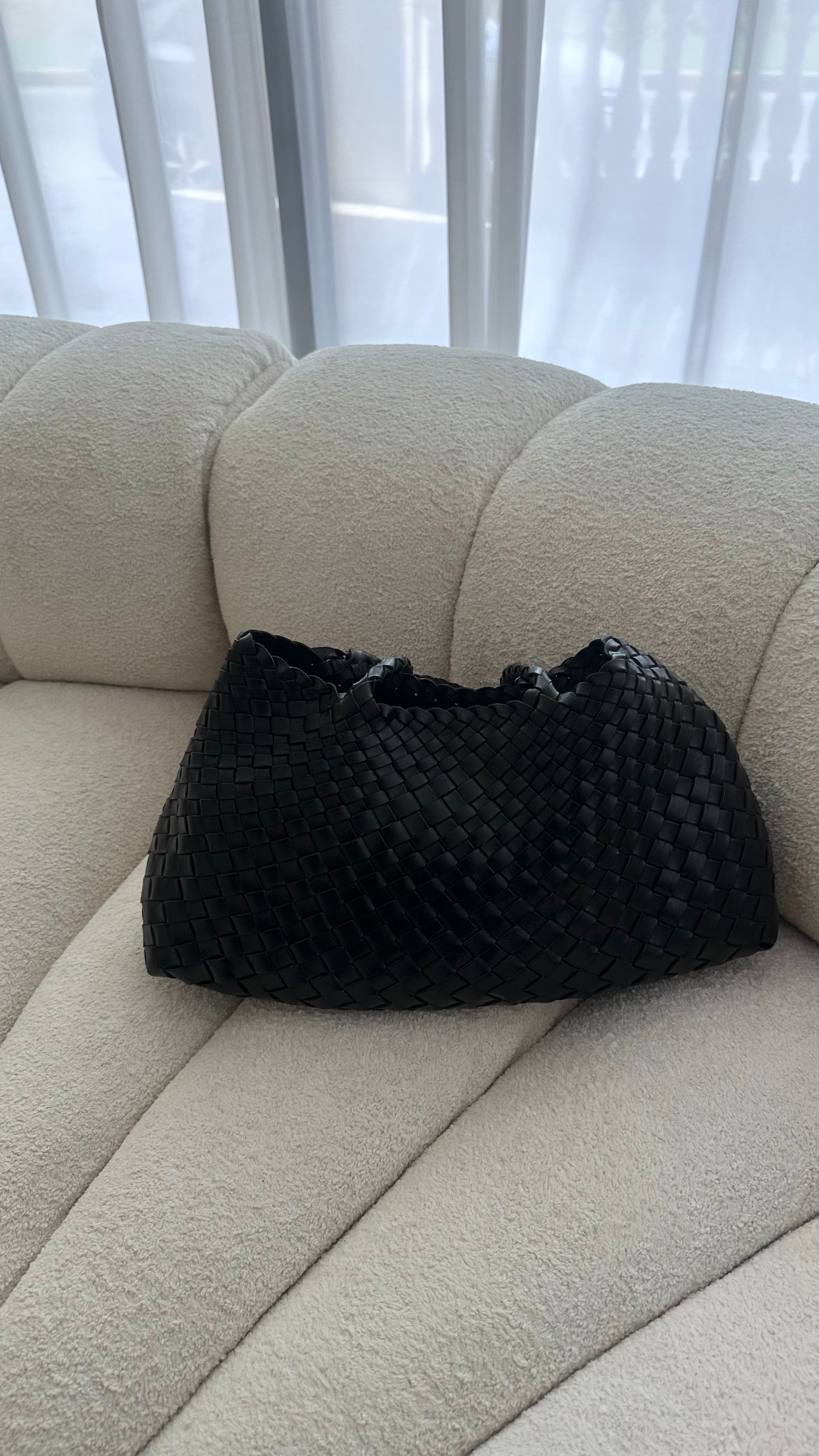 Black textured bag on a beige couch with a blurred window background