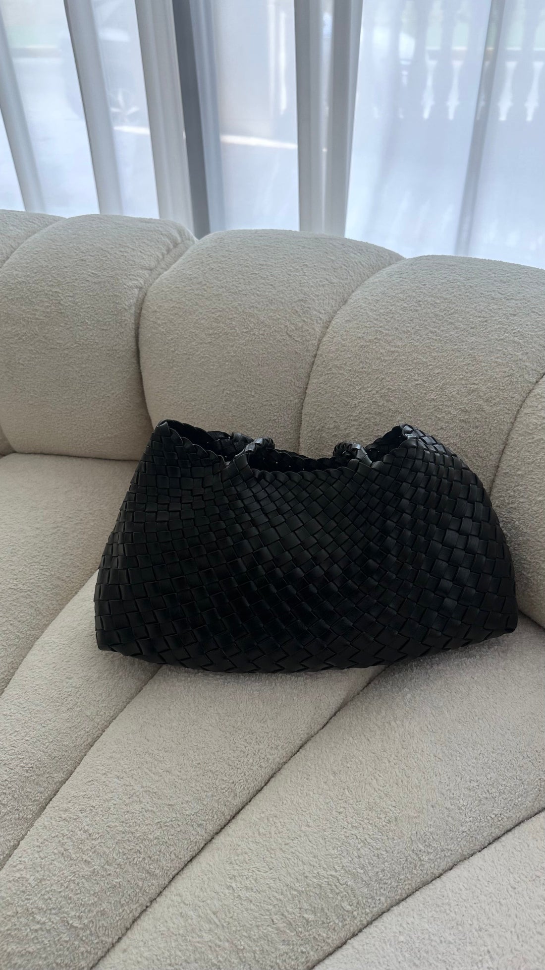 Black textured bag on a beige couch with a blurred window background