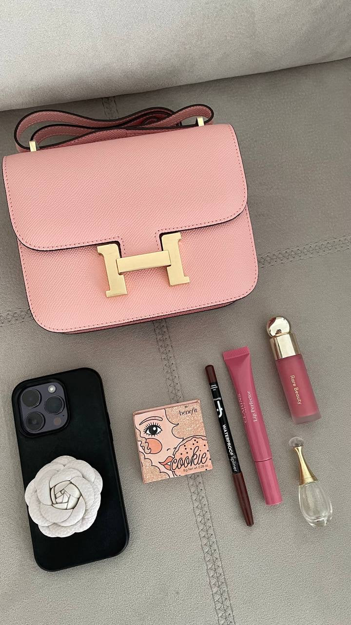 Pink handbag with makeup items including a phone, lip products, and a compact on a gray surface.