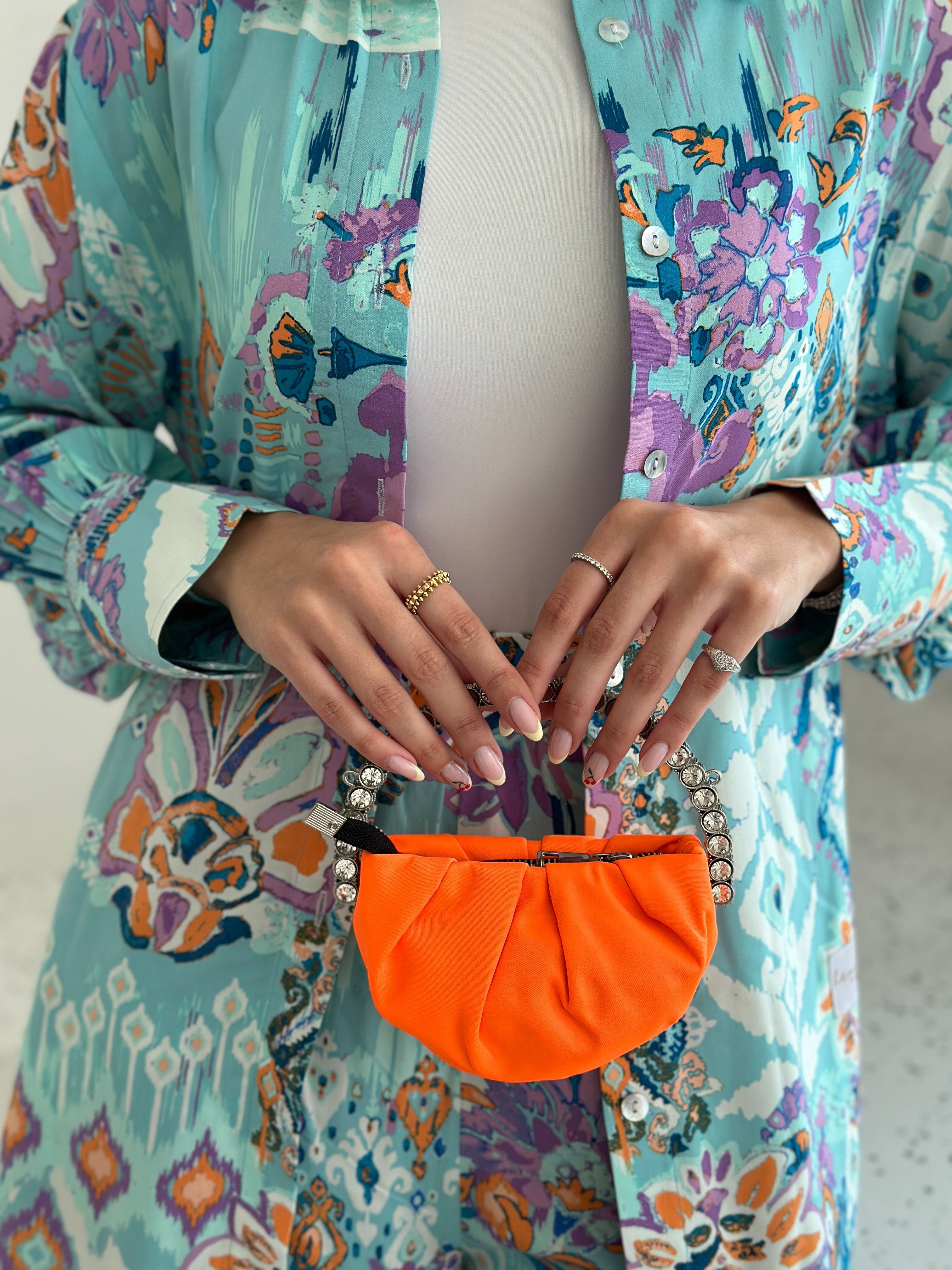 A person wearing a multicolored floral jacket holding a small orange handbag with a long chain.