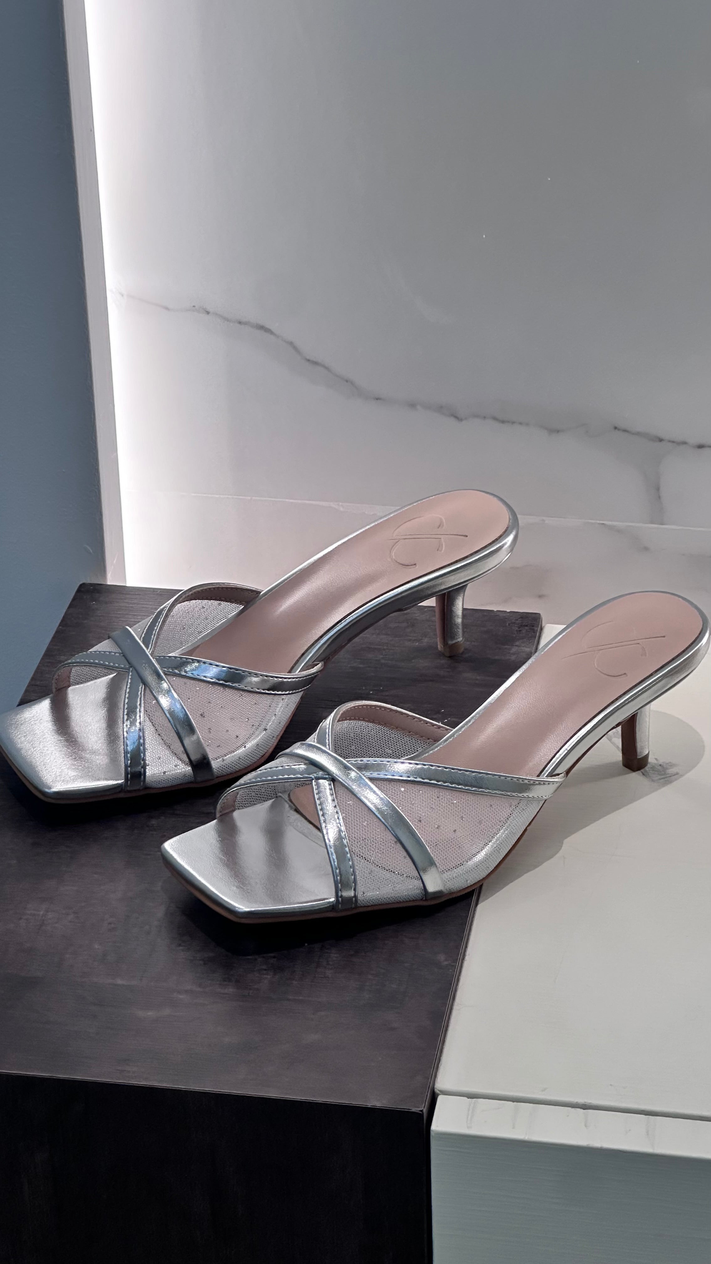 Silver high-heeled sandals on a black and white marble surface