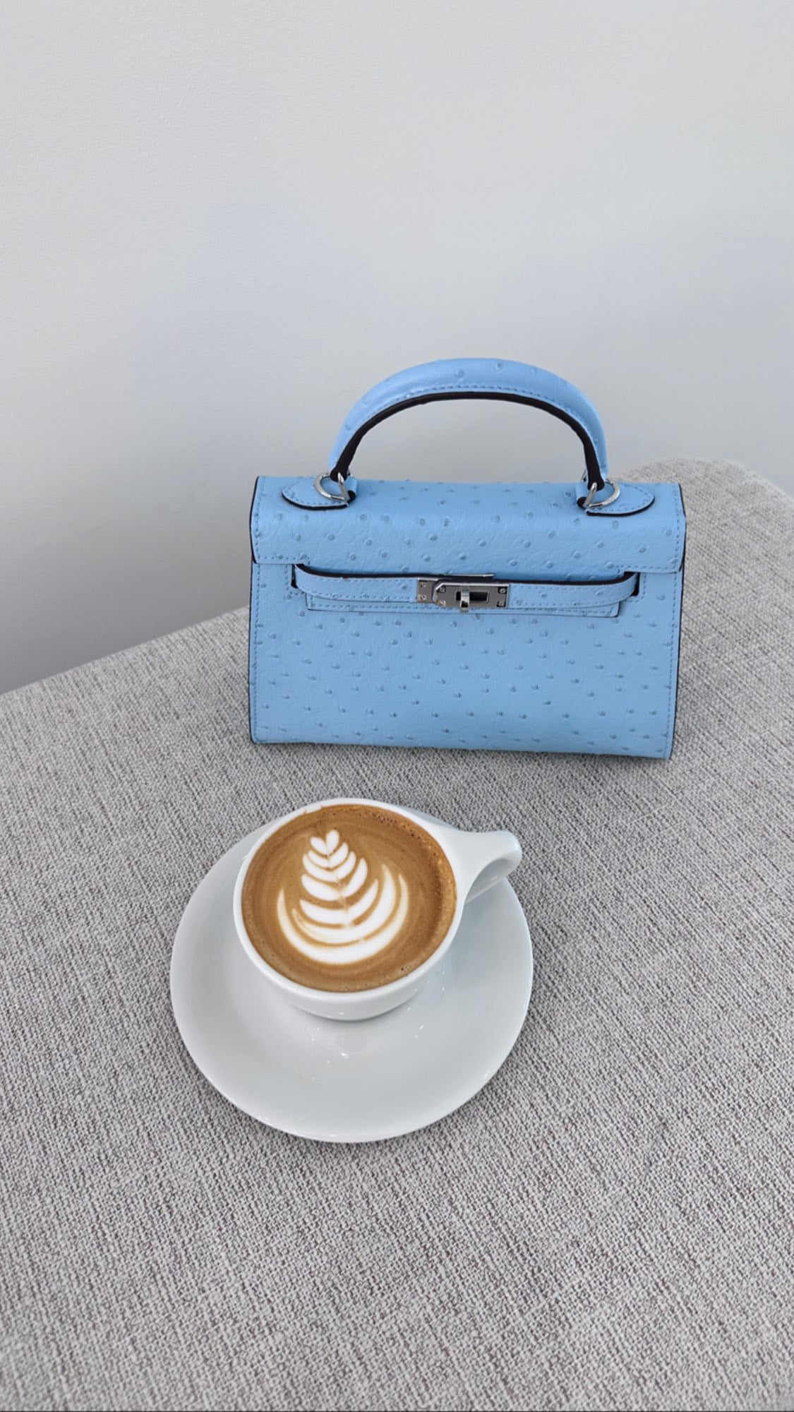 Blue handbag and cappuccino on a textured surface