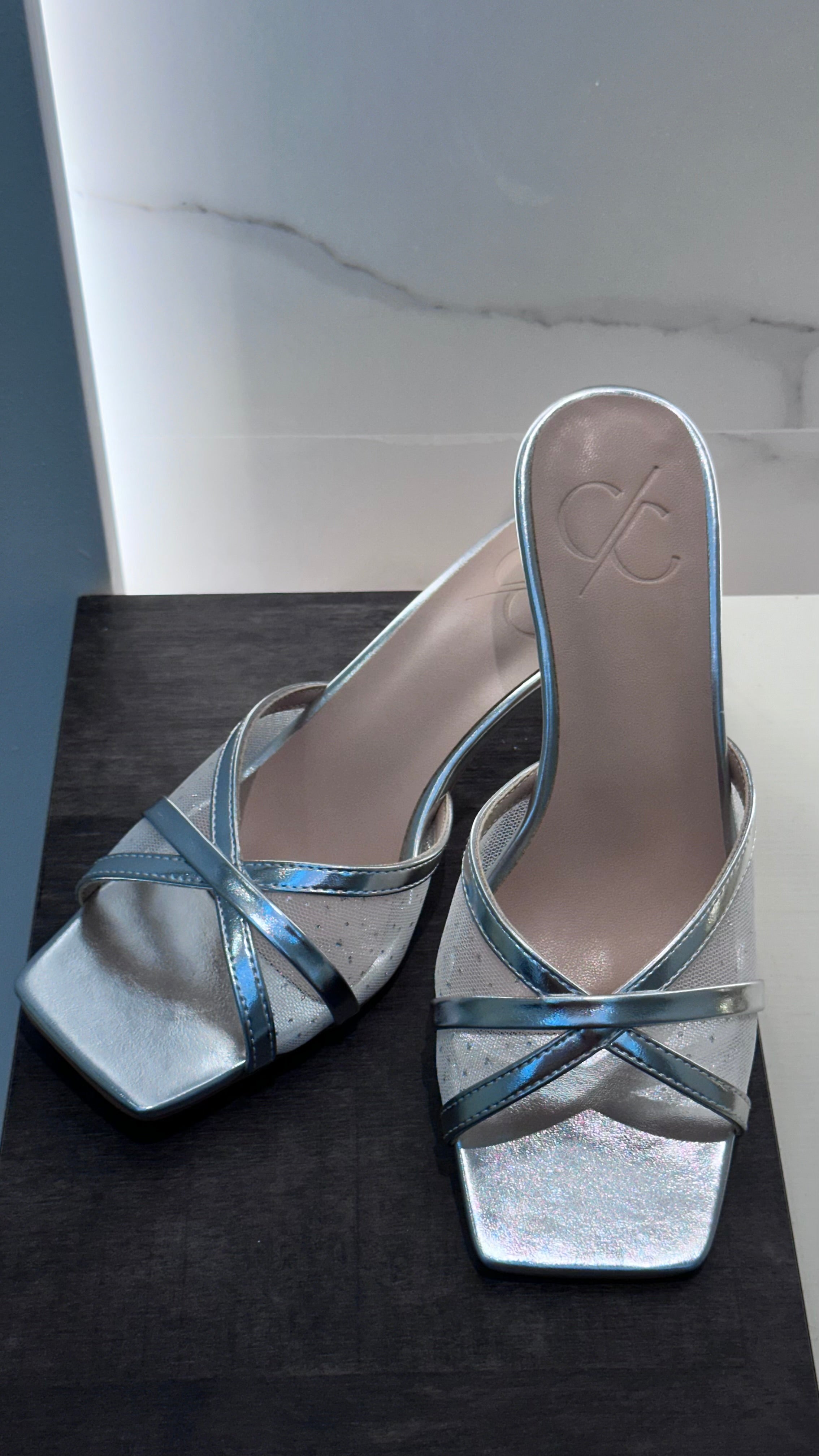 Silver high-heeled shoes with blue straps on a dark surface