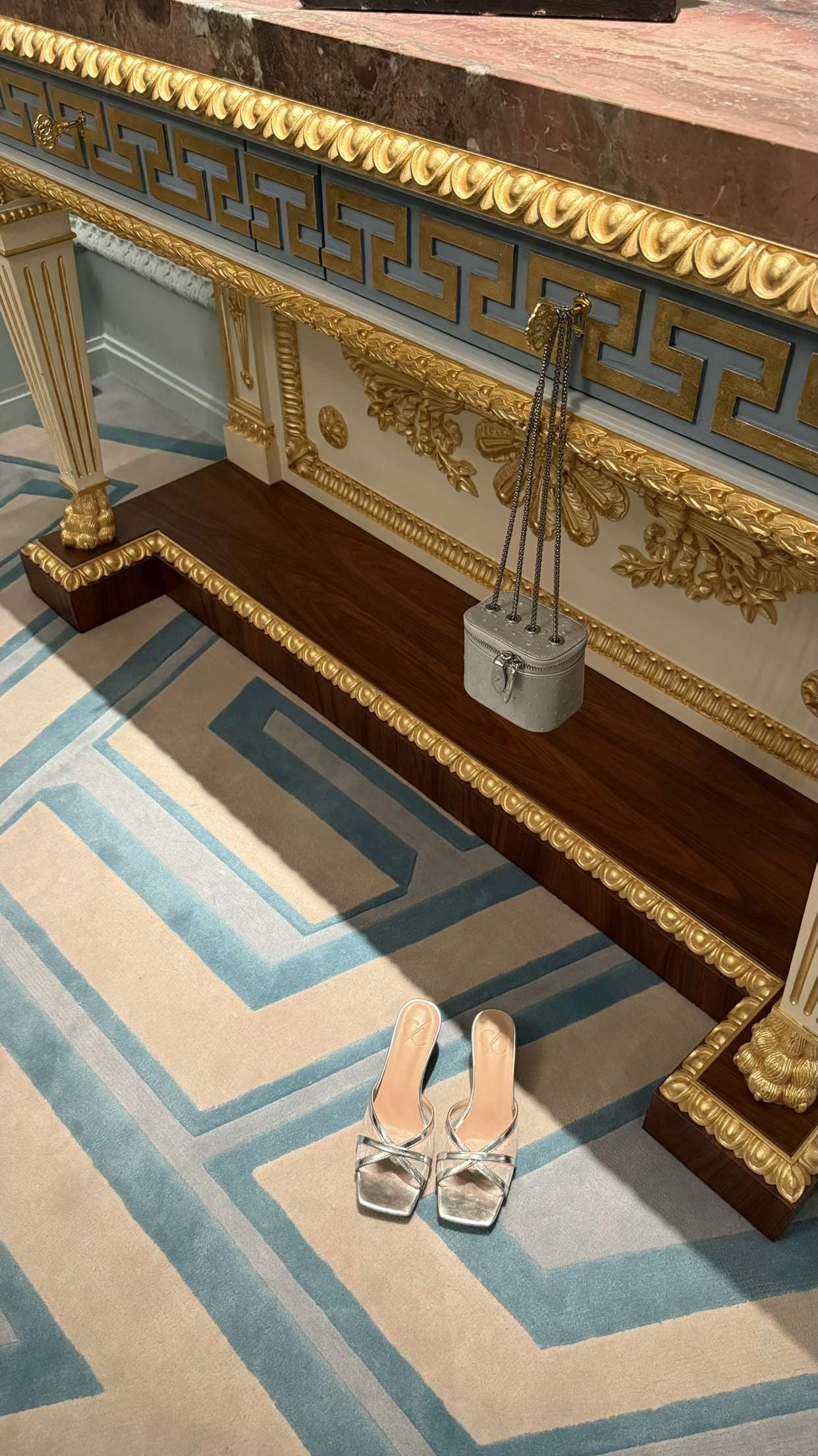 Decorative fireplace with gold accents and a pair of silver shoes on a patterned rug.