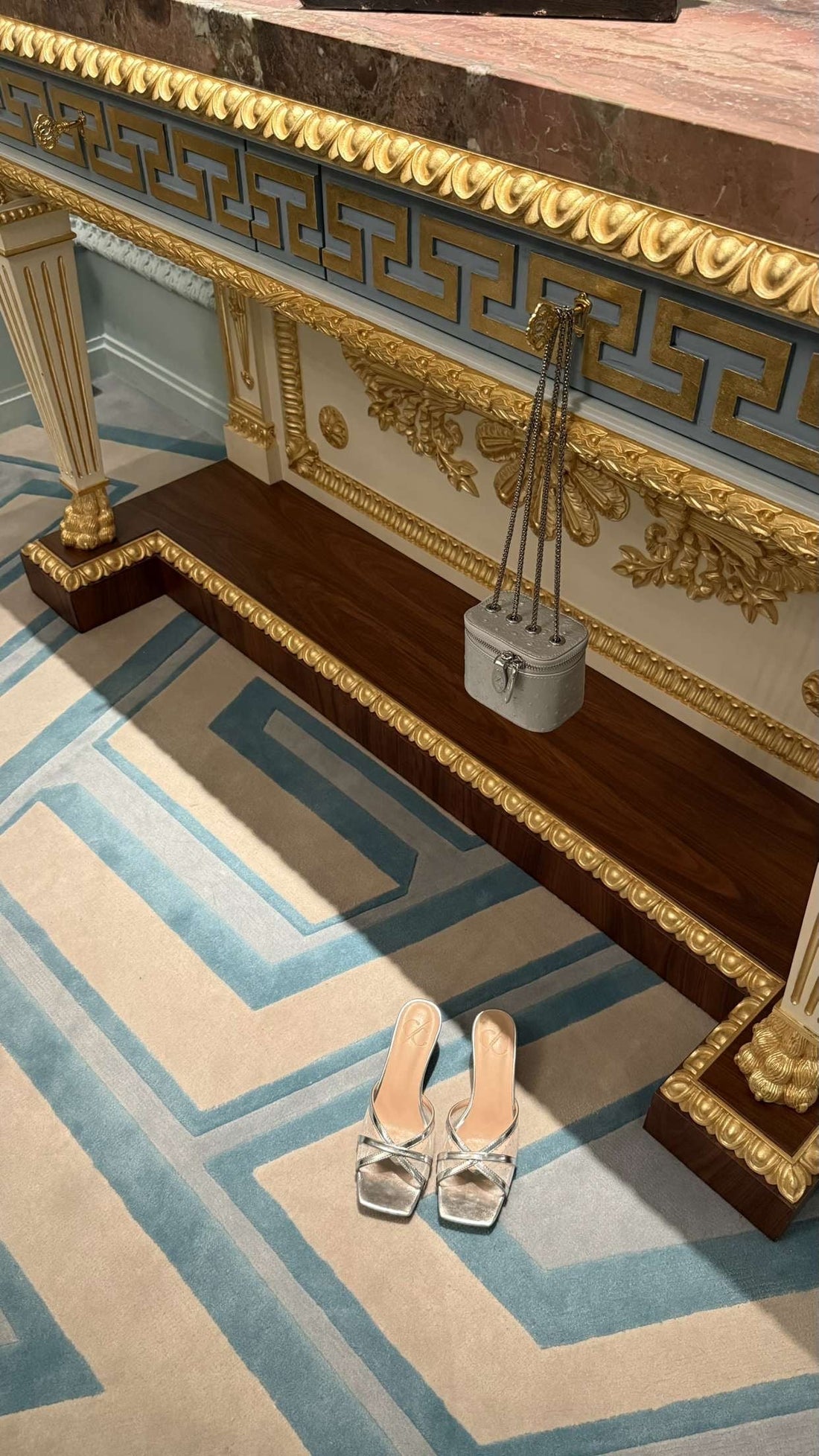 Decorative fireplace with gold accents and a pair of silver shoes on a patterned rug.