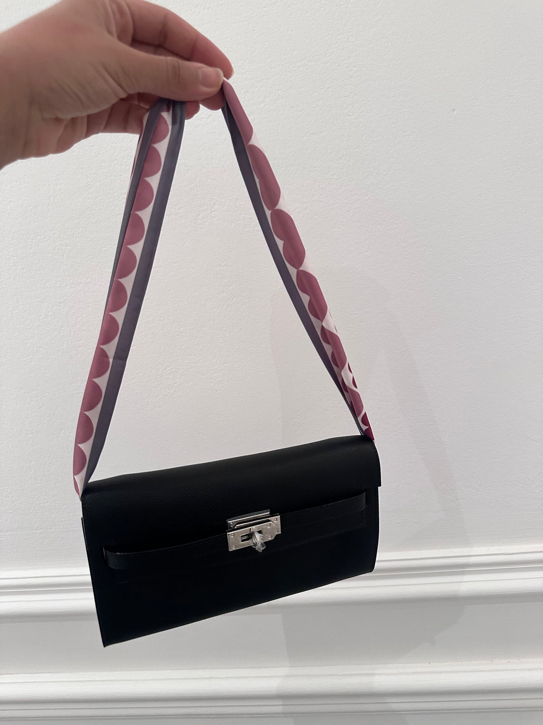 Black handbag with a patterned strap held by a hand against a white background