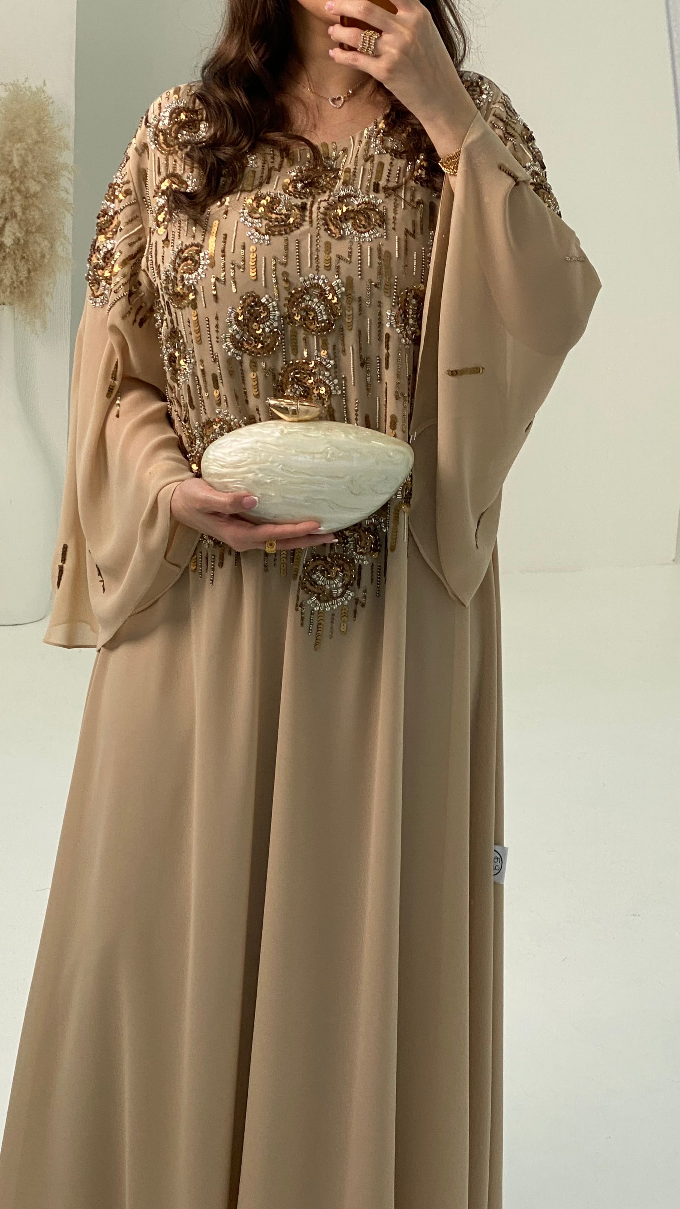 Woman wearing a beige dress with gold embroidery holding a white bowl.