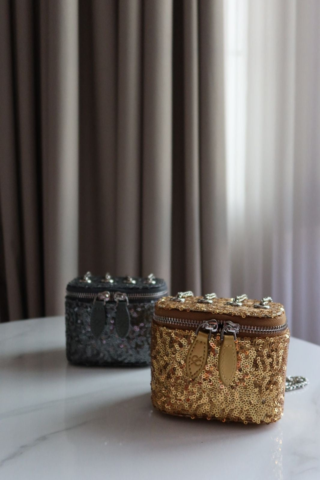 Two glittery pouches, one gold and one black, on a marble surface with curtains in the background.