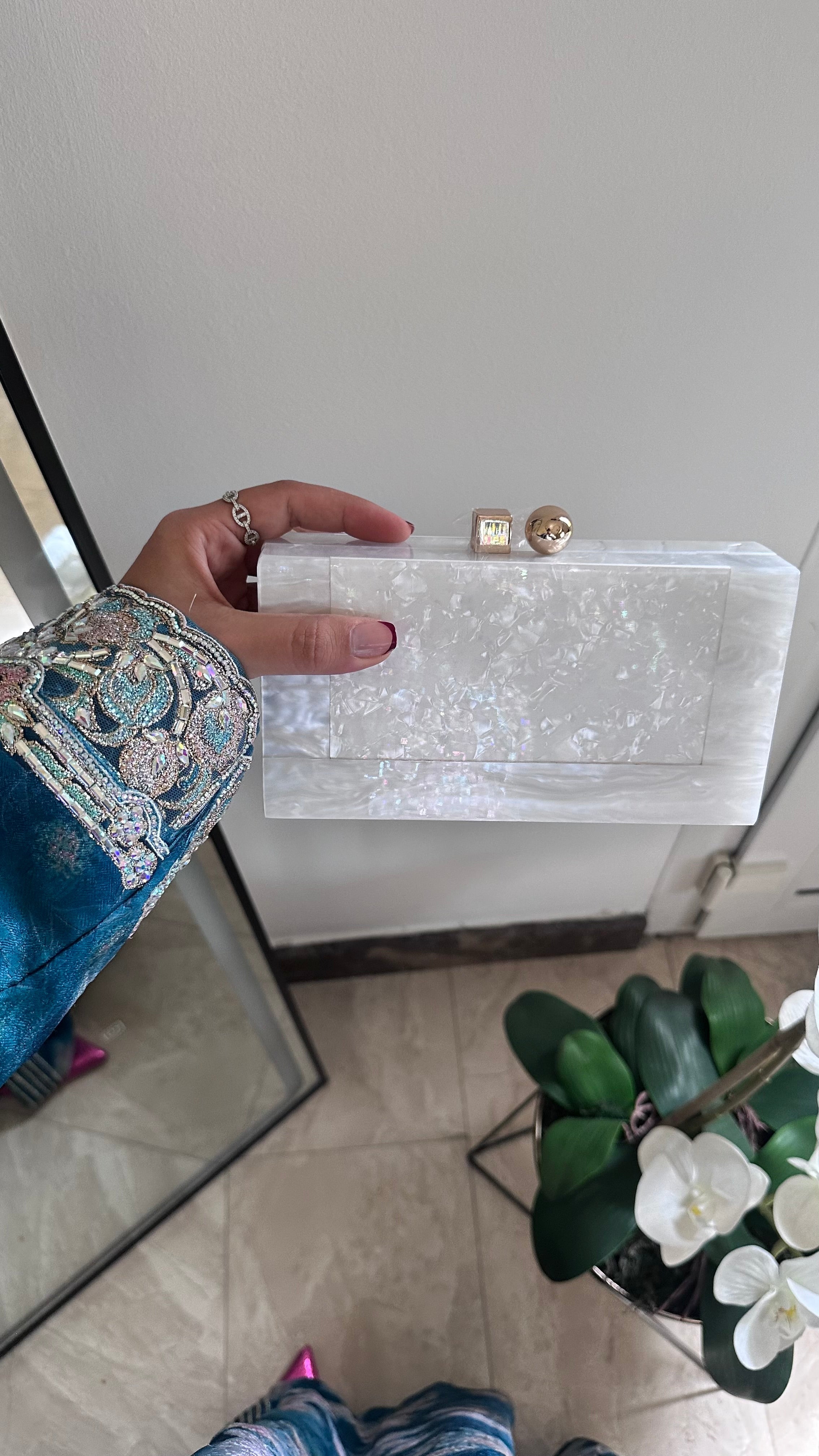 Hand holding a white clutch bag with gold accents against a neutral background