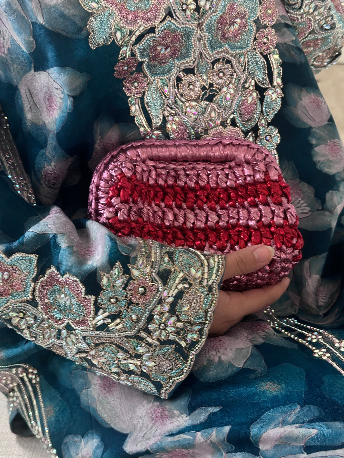 Decorative clutch with intricate patterns held by a hand against a floral fabric background