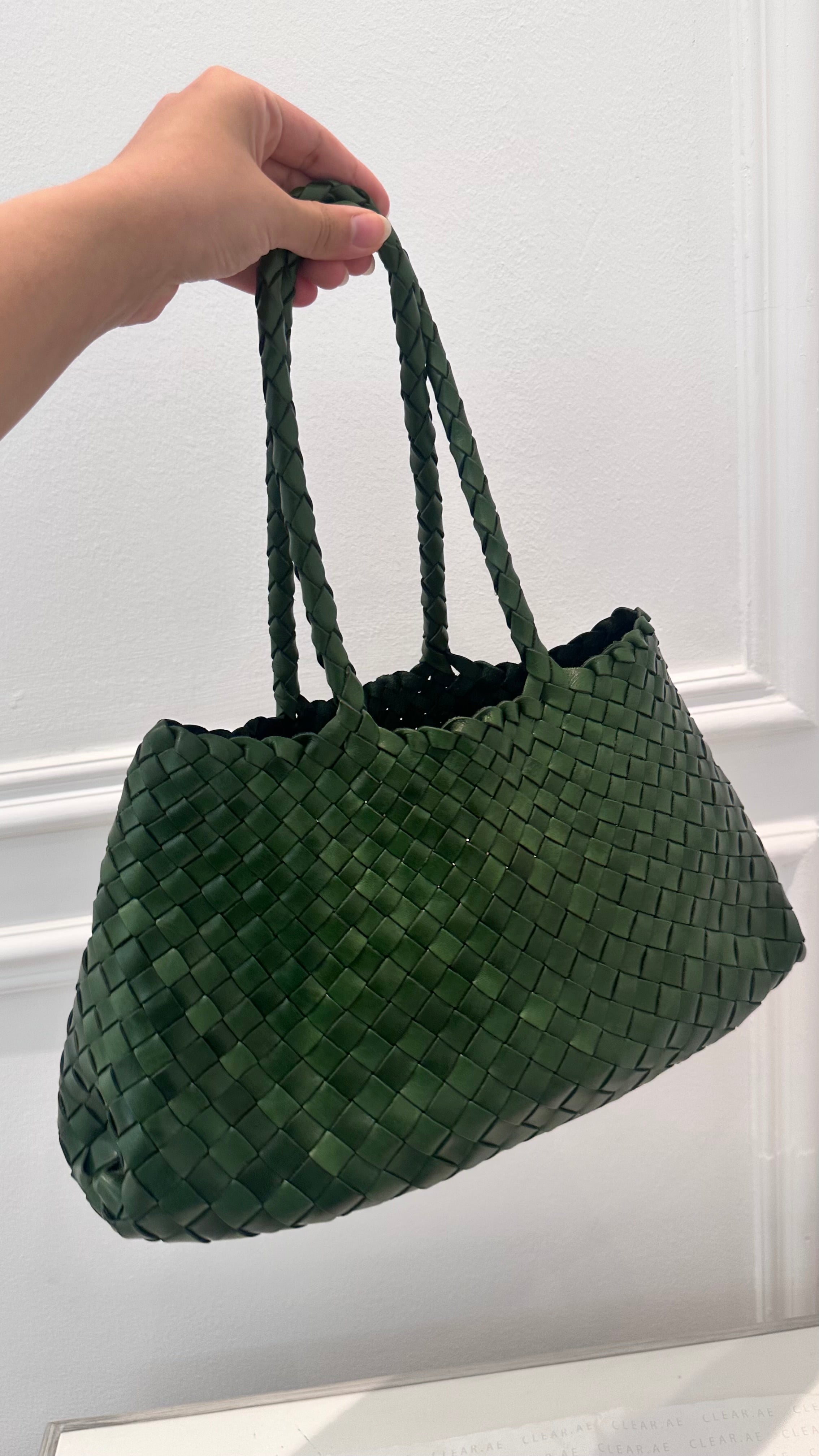 Green woven handbag held by a hand against a white background