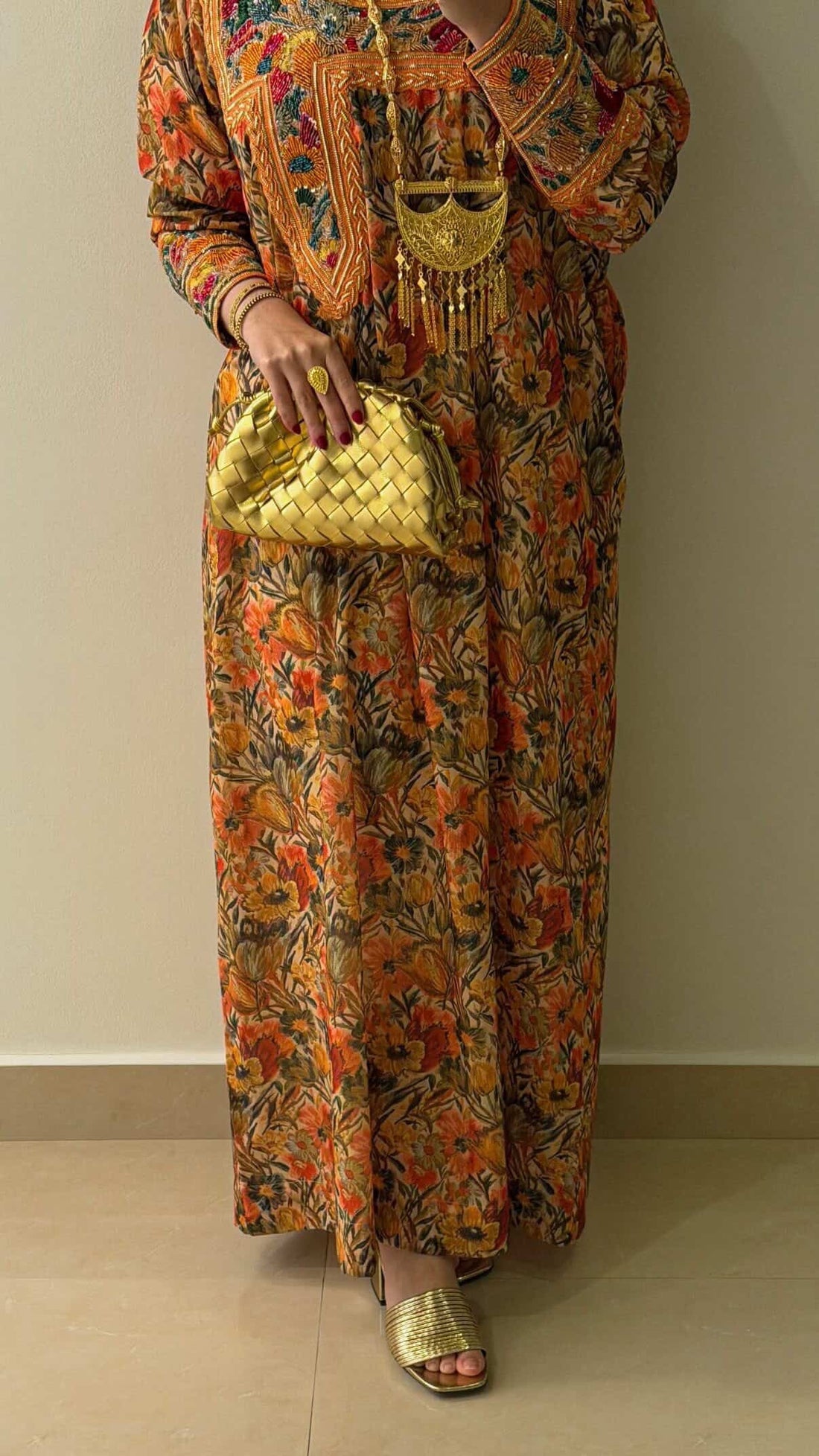 Person wearing a colorful floral outfit with a gold handbag against a plain background