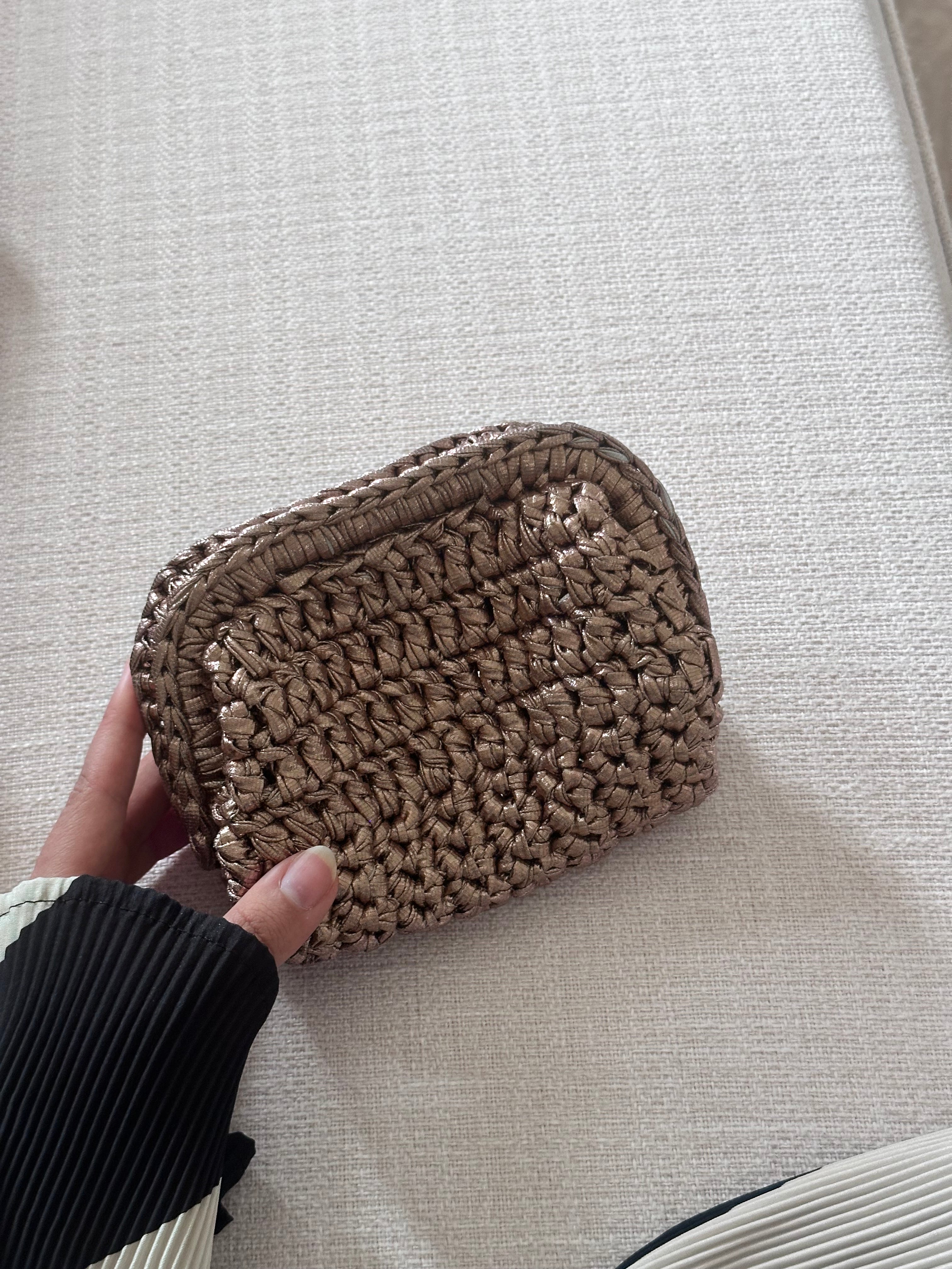 Hand holding a woven beige pouch on a light gray surface