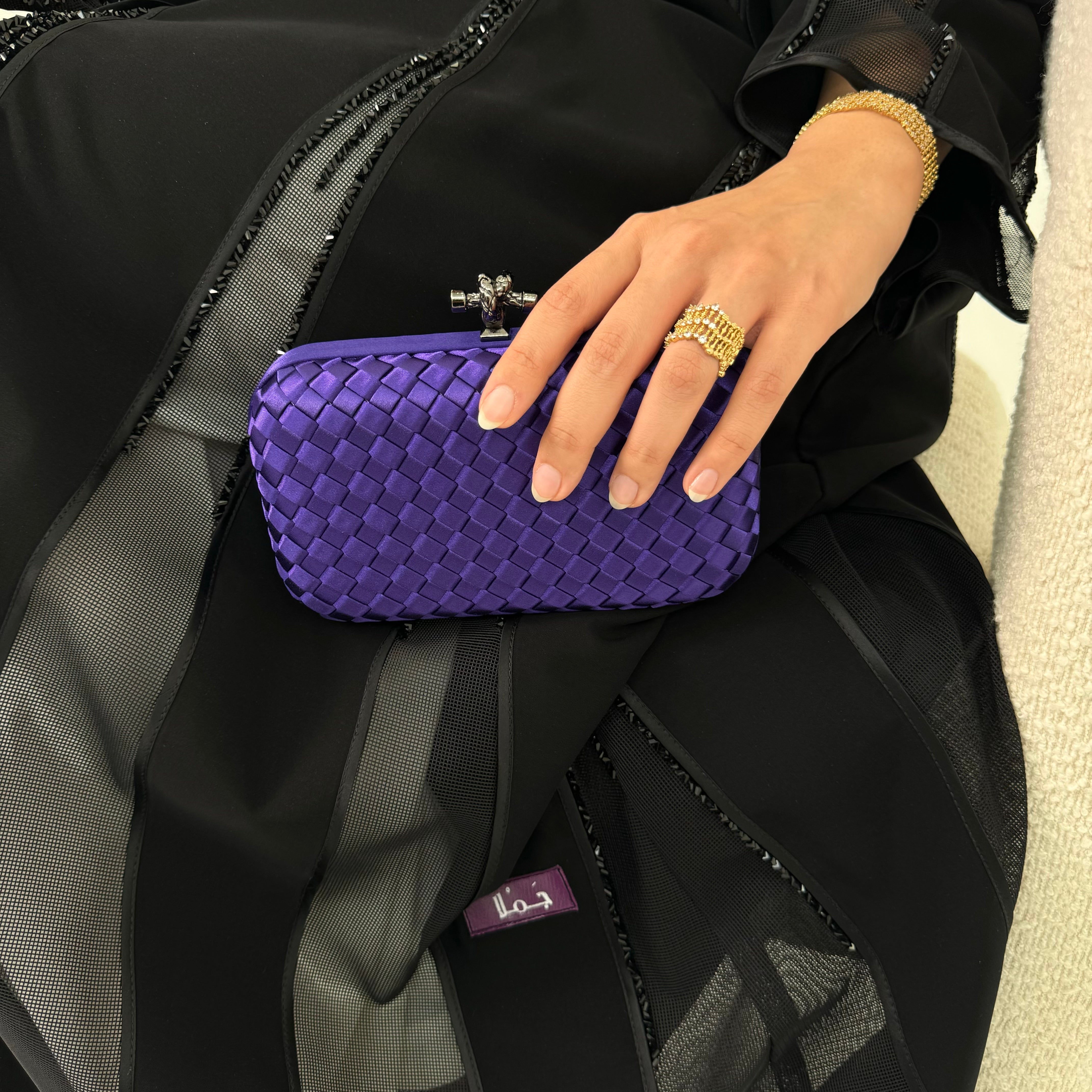 A person holding a dark purple clutch purse with a textured surface and a metallic clasp.