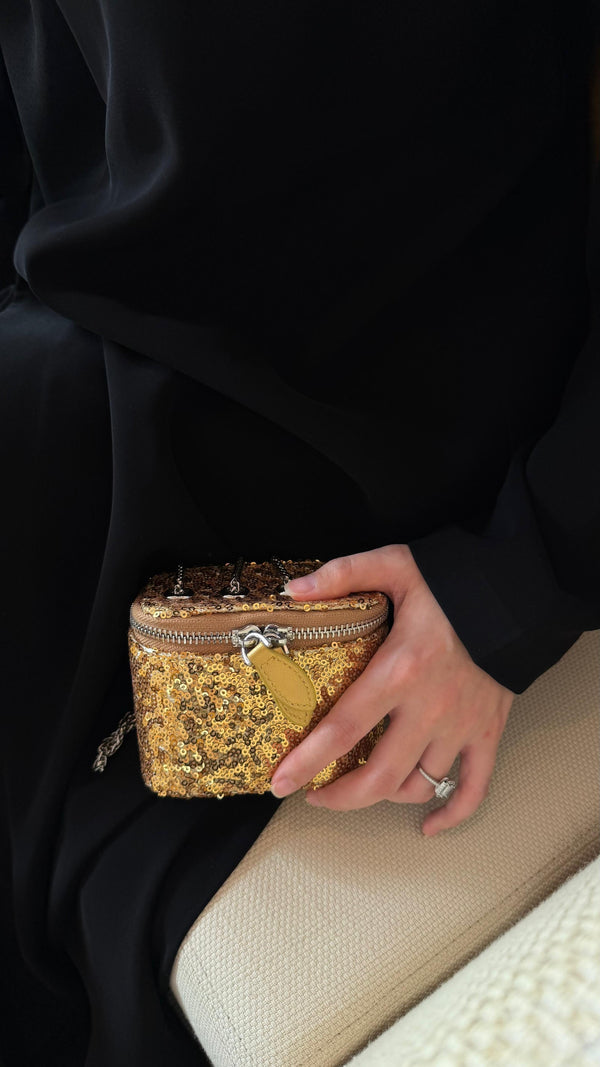 Person holding a gold sequined clutch bag with a beige surface underneath