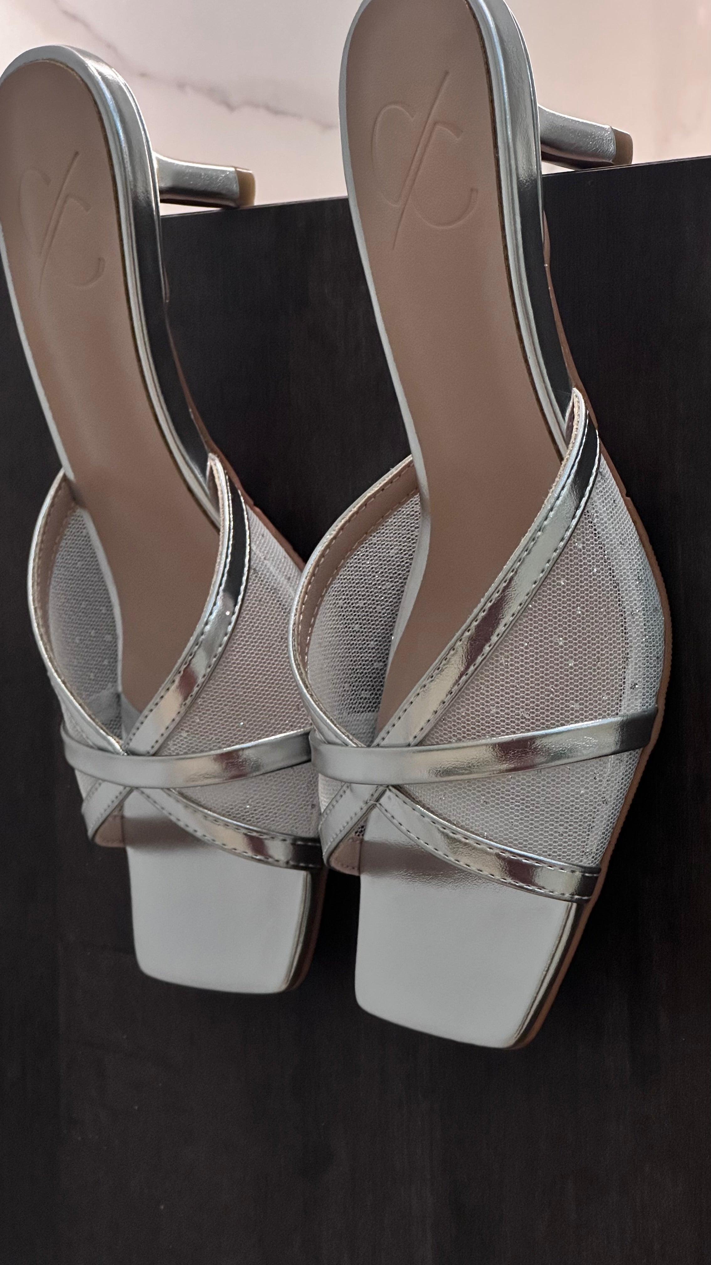 Silver high-heeled shoes with criss-cross straps on a black background