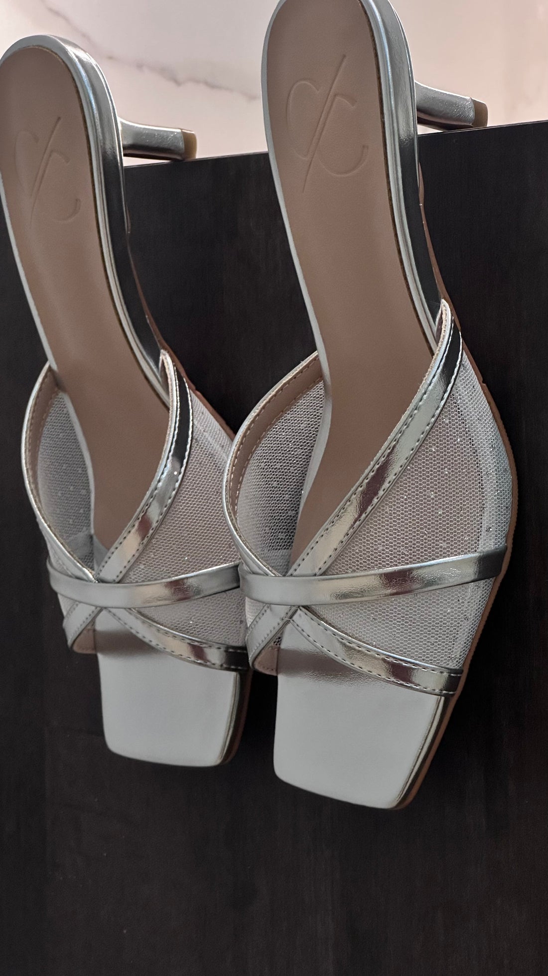 Silver high-heeled shoes with criss-cross straps on a black background