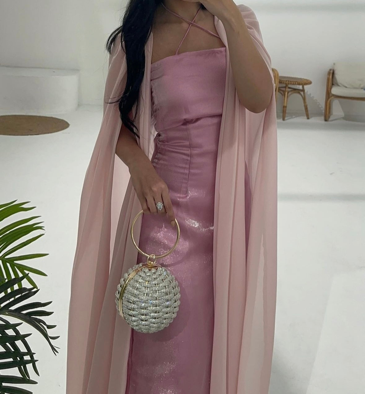 A person in a pink dress holding a round, gold-colored bag with a glossy finish.