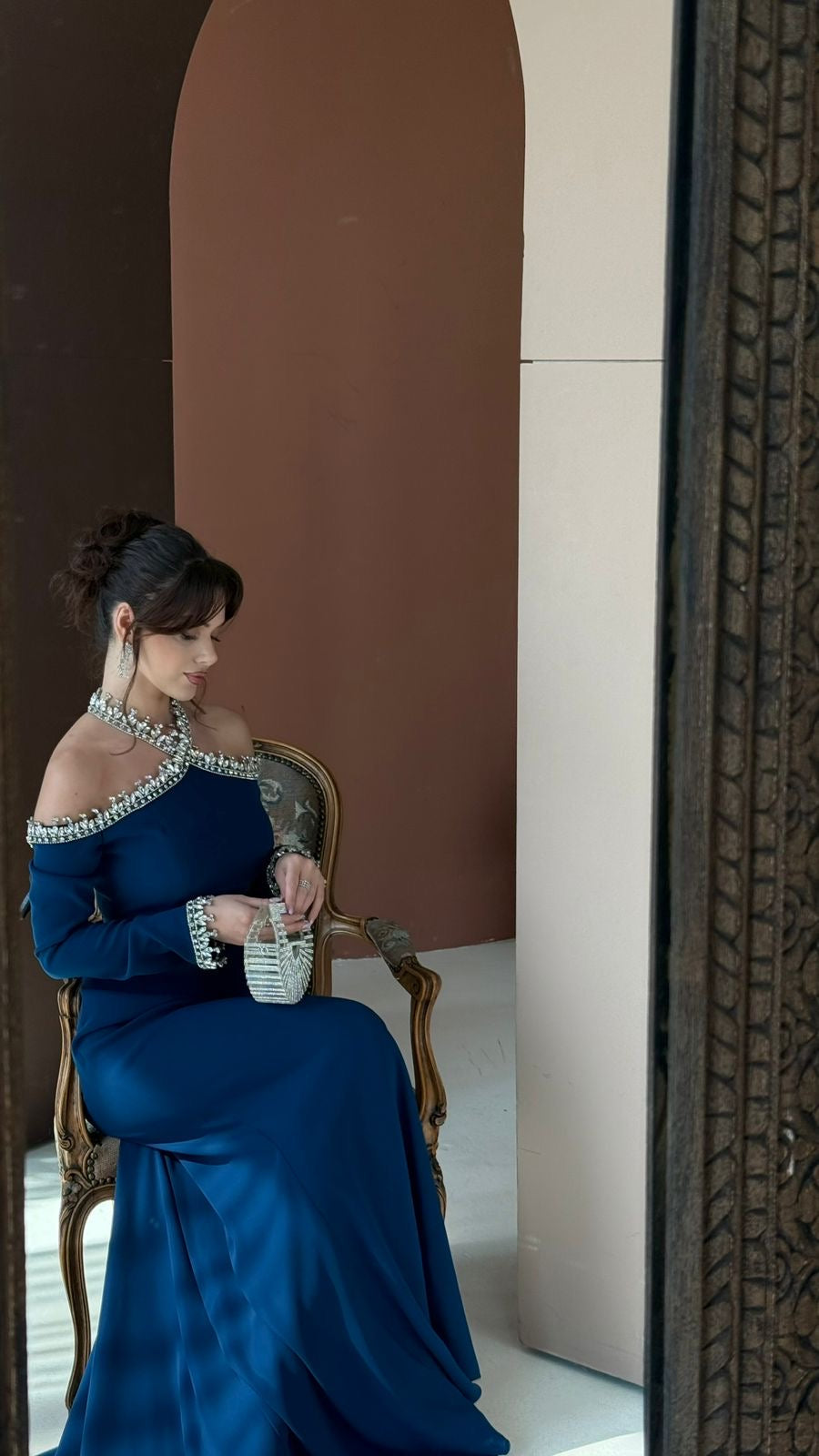 Woman in a blue dress sitting on a chair in a room with a decorative wall.