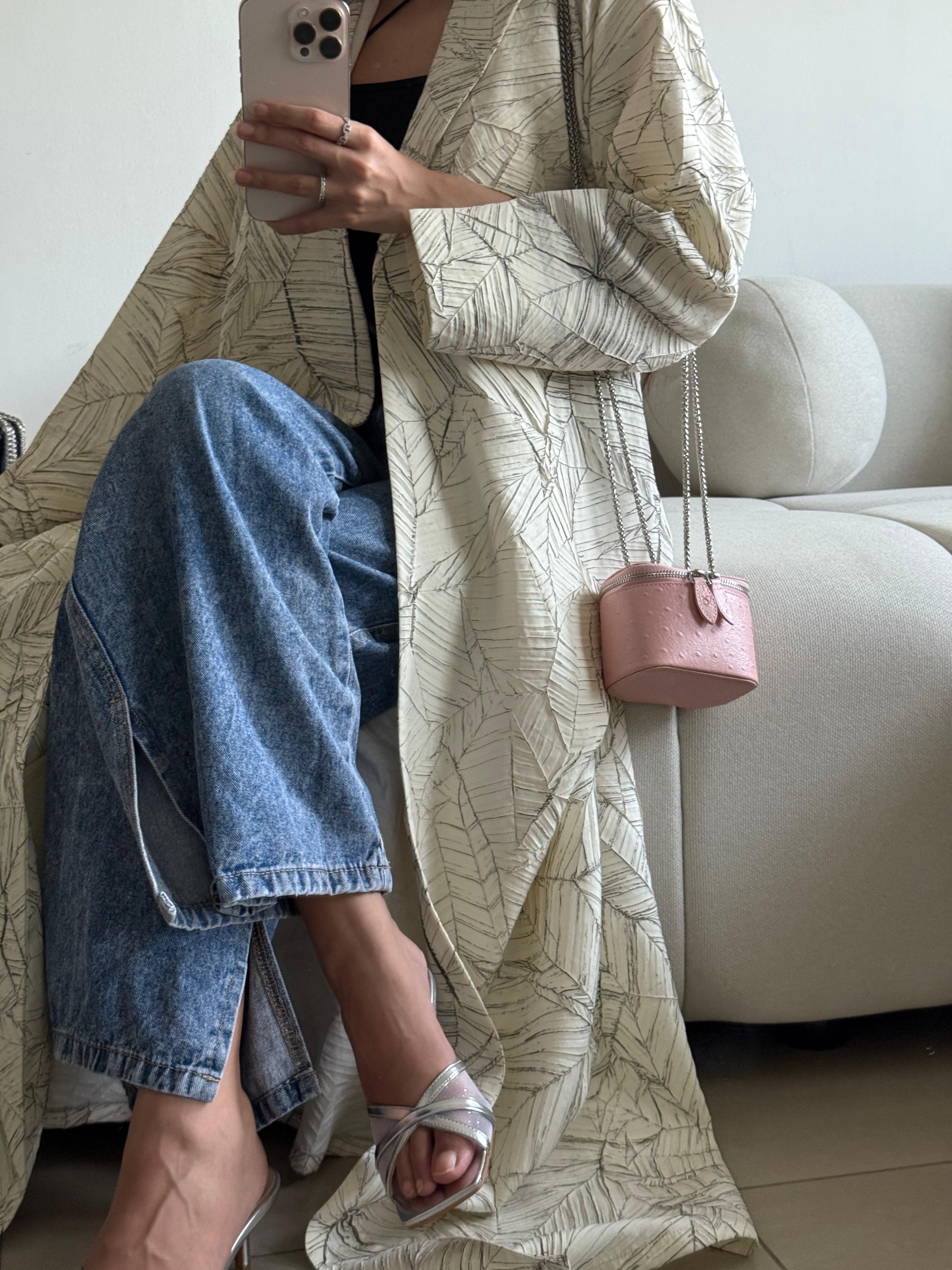 Person wearing a long beige coat sitting on a couch with a pink handbag.