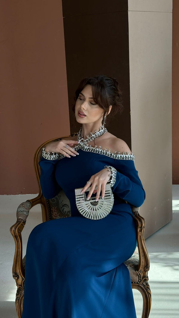 Woman in a blue evening gown sitting on a chair with a neutral background