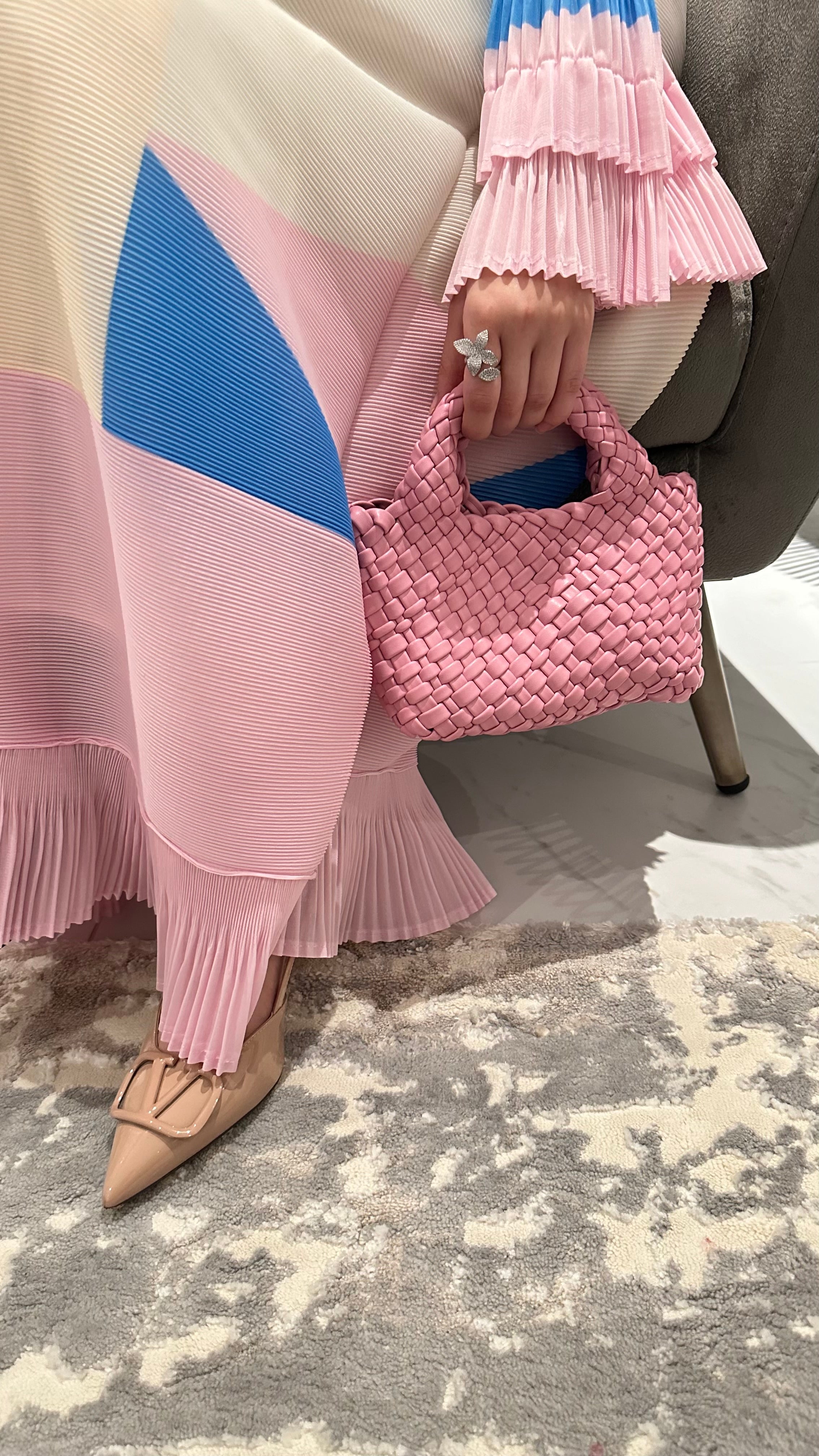 A close-up of a person's hand holding a pink, textured handbag.