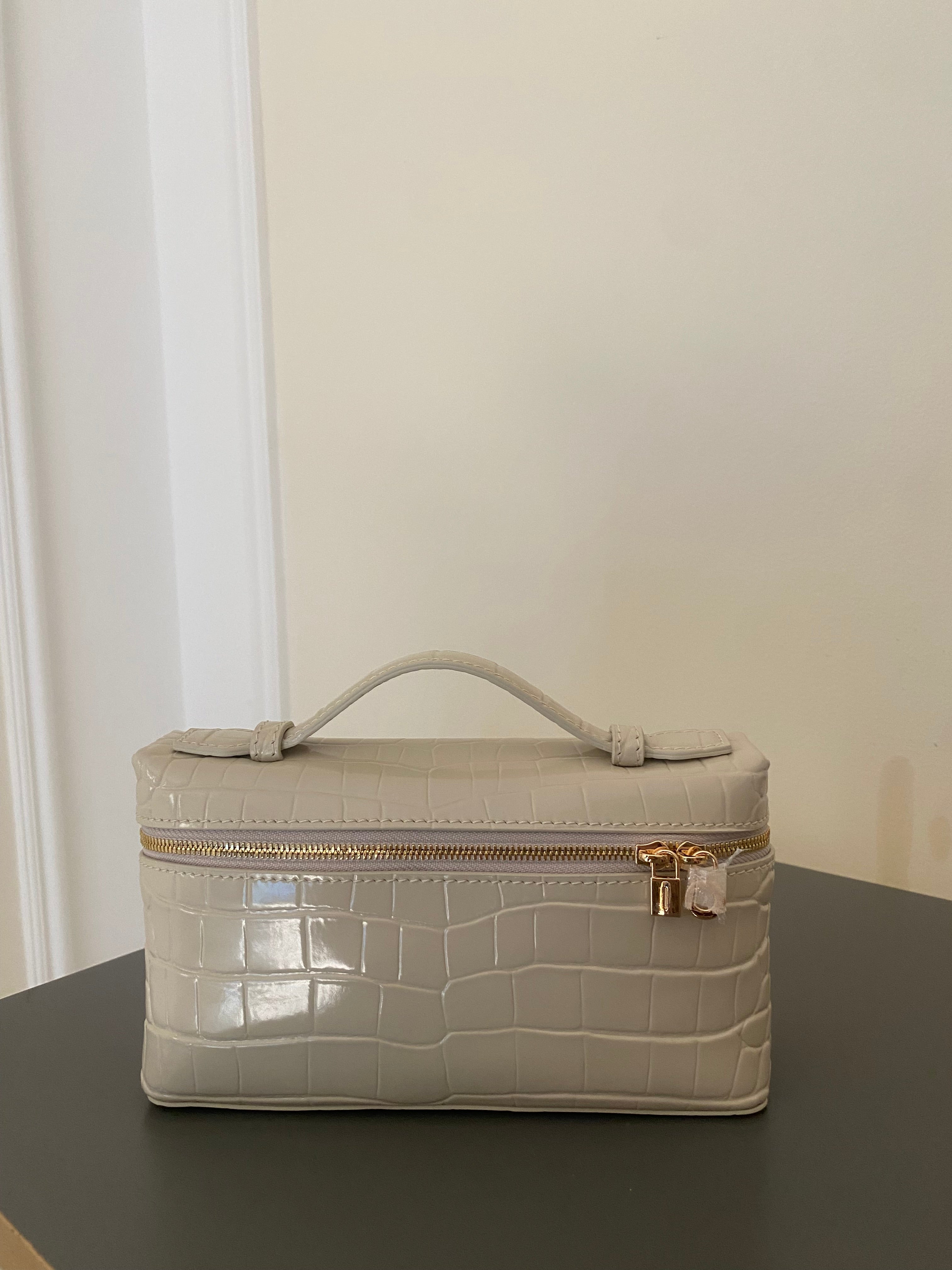 Beige crocodile-patterned suitcase on a dark surface with a light background