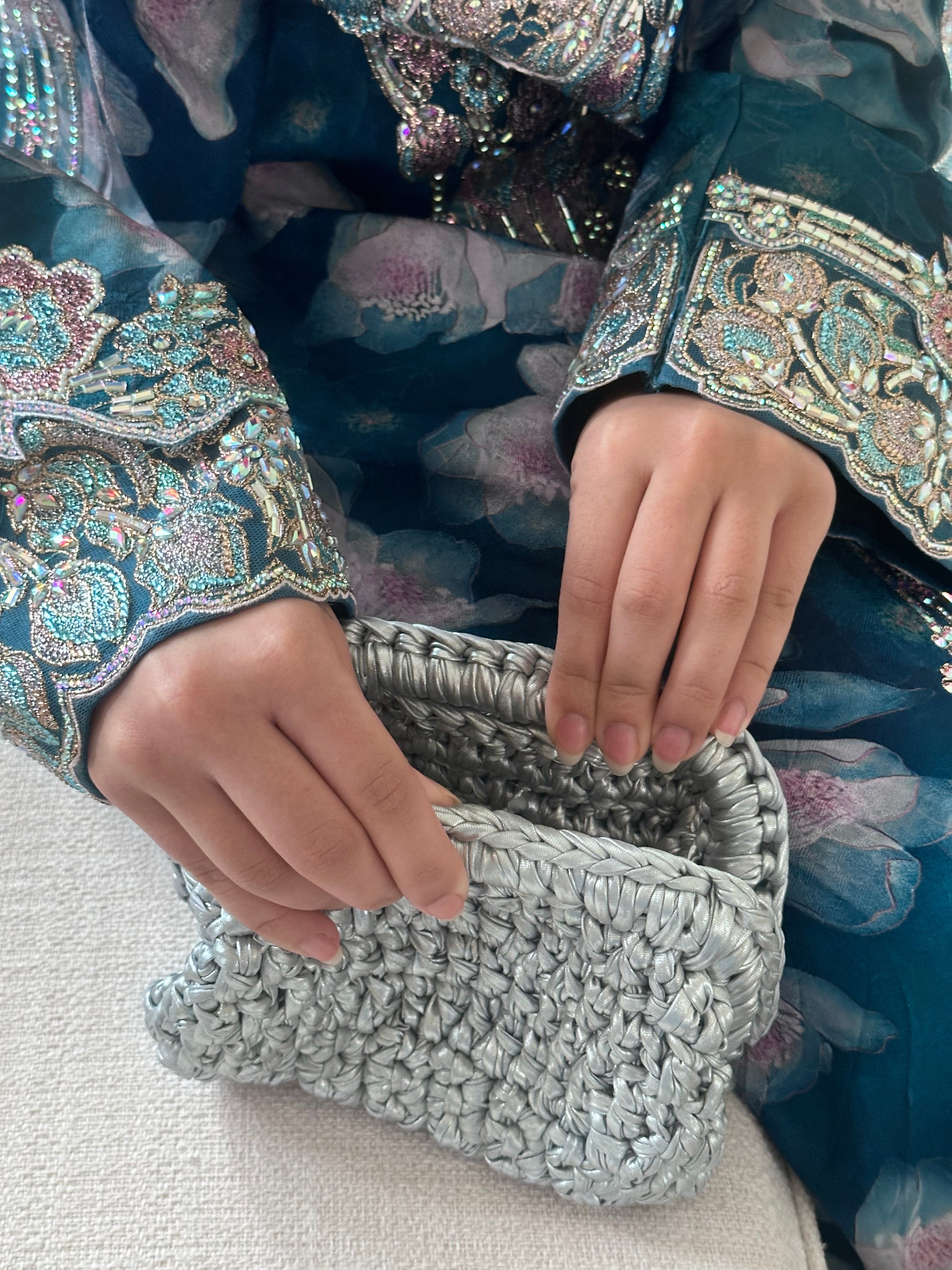 Person wearing a decorative outfit with intricate patterns, holding a silver textured clutch.
