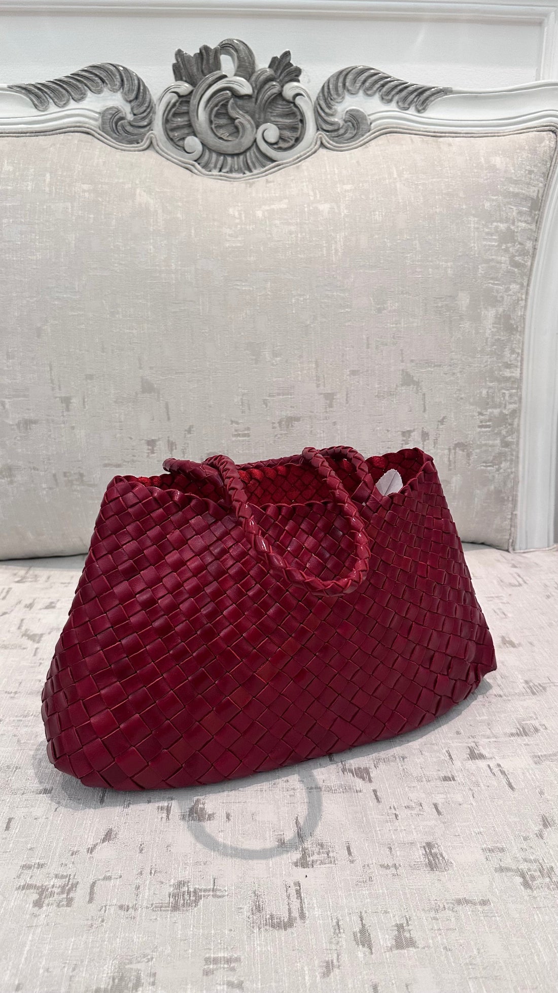 Red velvet handbag on a textured surface with decorative headboard in the background