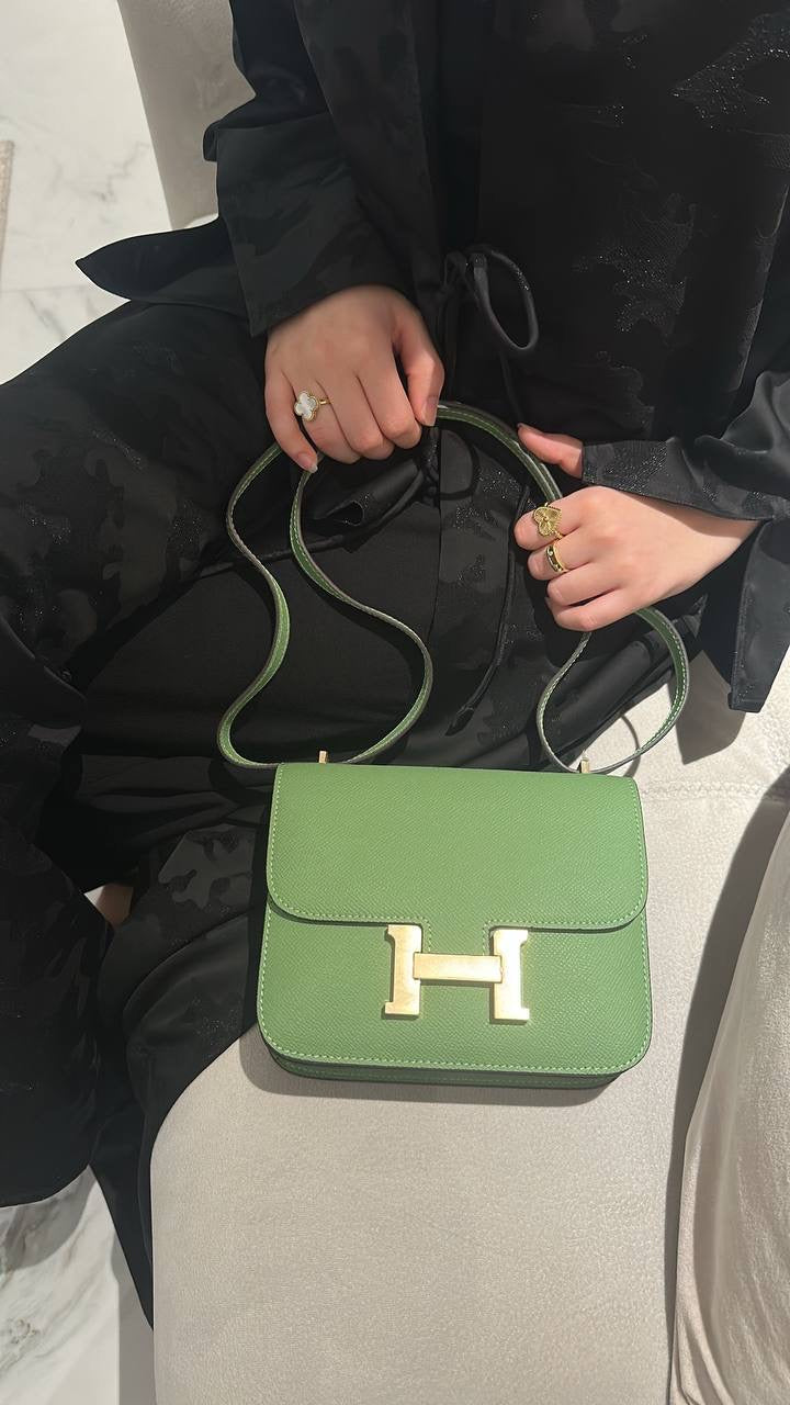 A person sitting with a green handbag with a gold-tone logo on it.