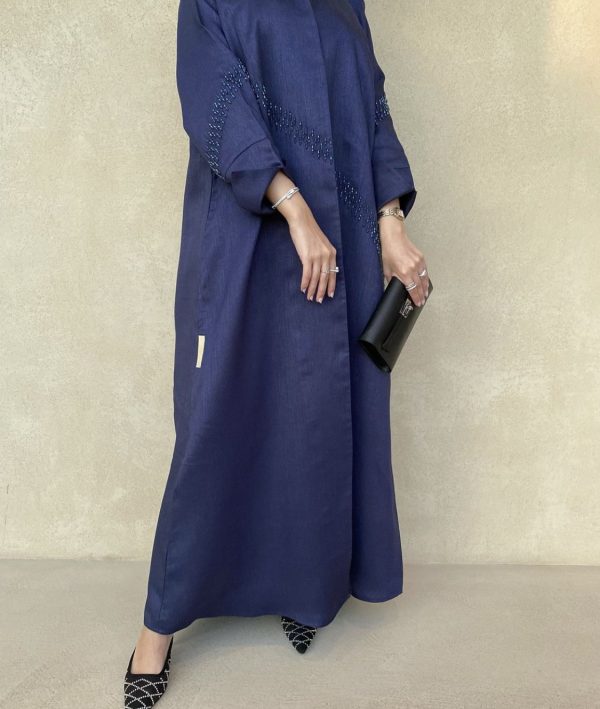 Person wearing a long blue dress with intricate detailing against a plain background