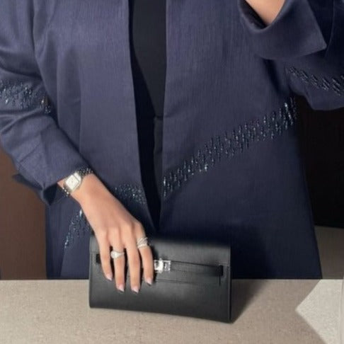 Person wearing a dark blue outfit with beaded details, holding a black clutch.