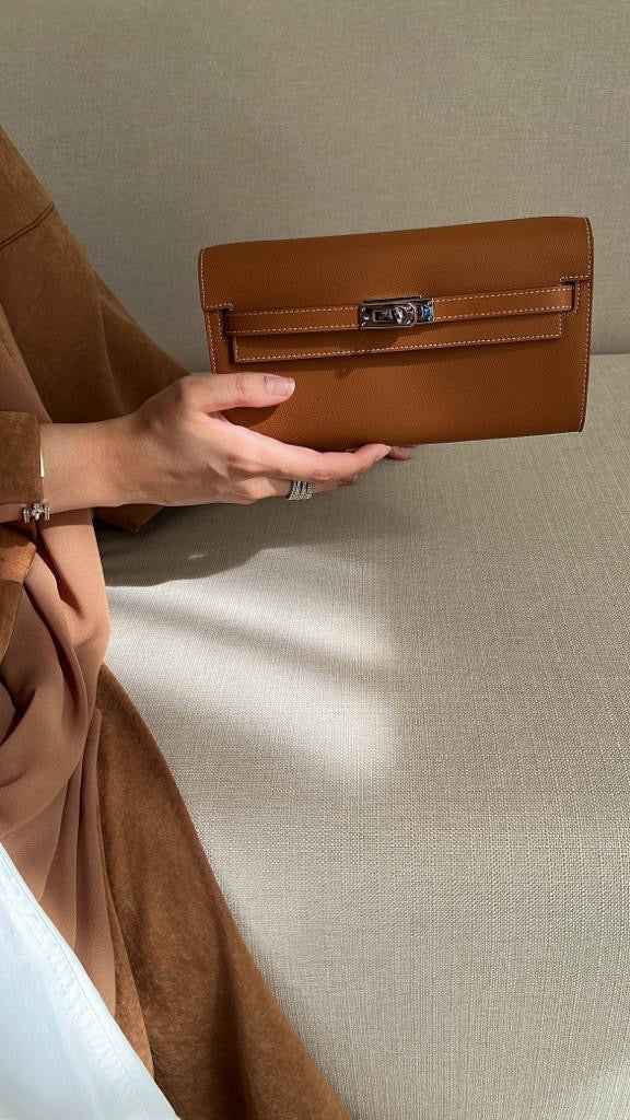 Person holding a brown clutch bag against a neutral background