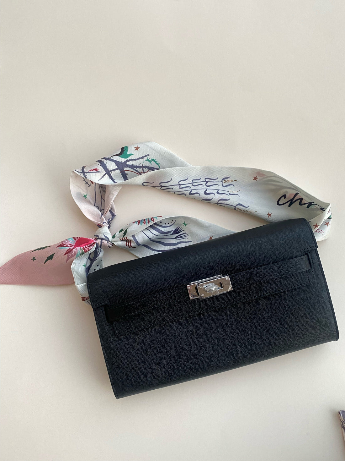 Black handbag with a floral scarf draped over it on a light background