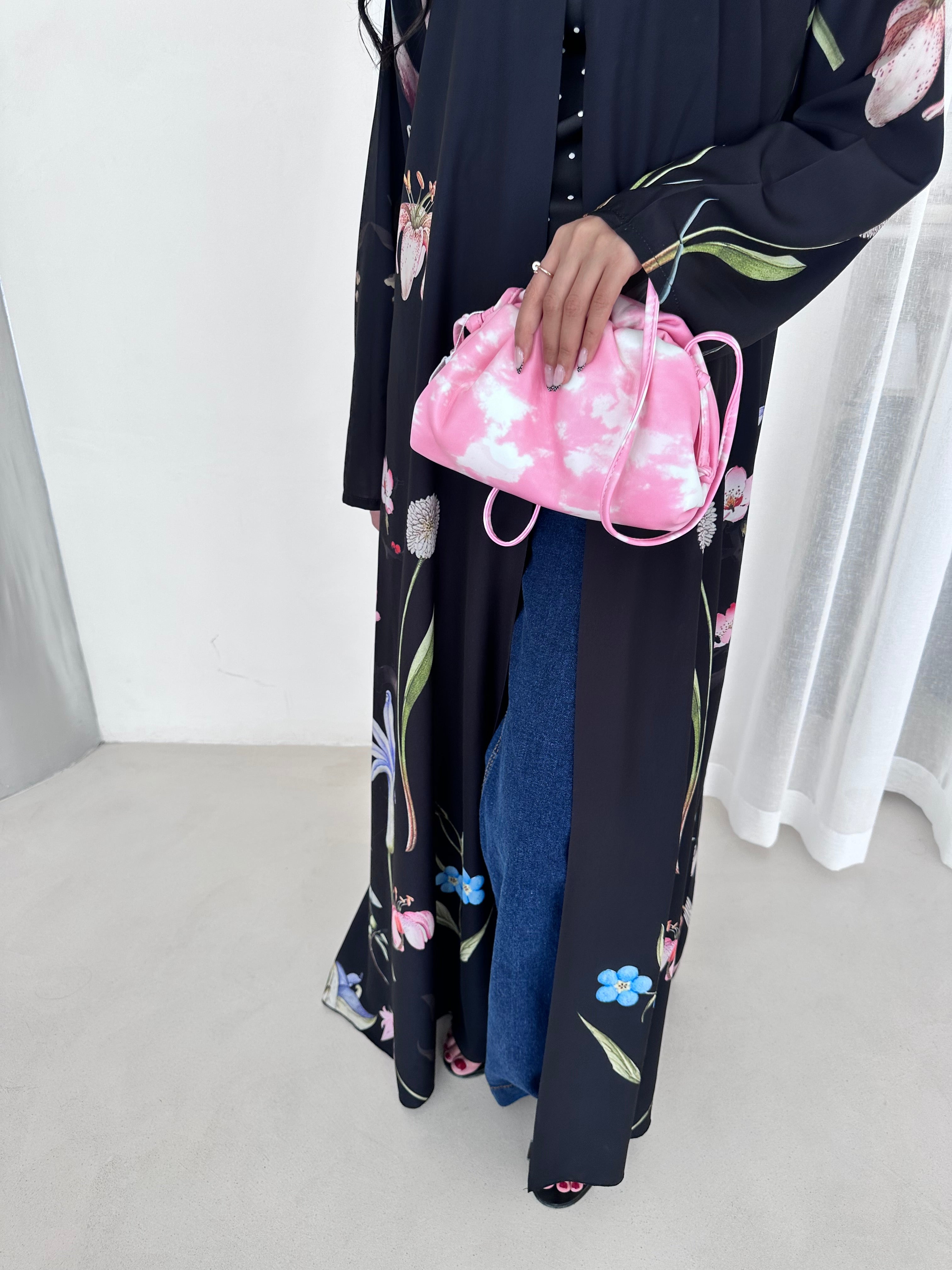 Person holding a pink bag with floral design against a white curtain background