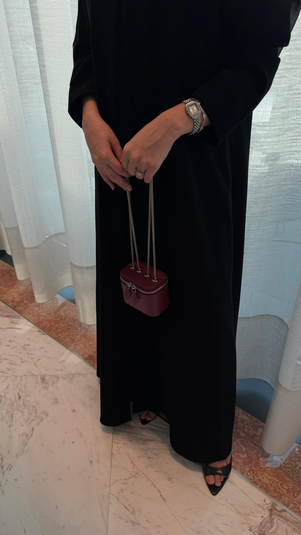 Person wearing a black outfit holding a small red handbag indoors.
