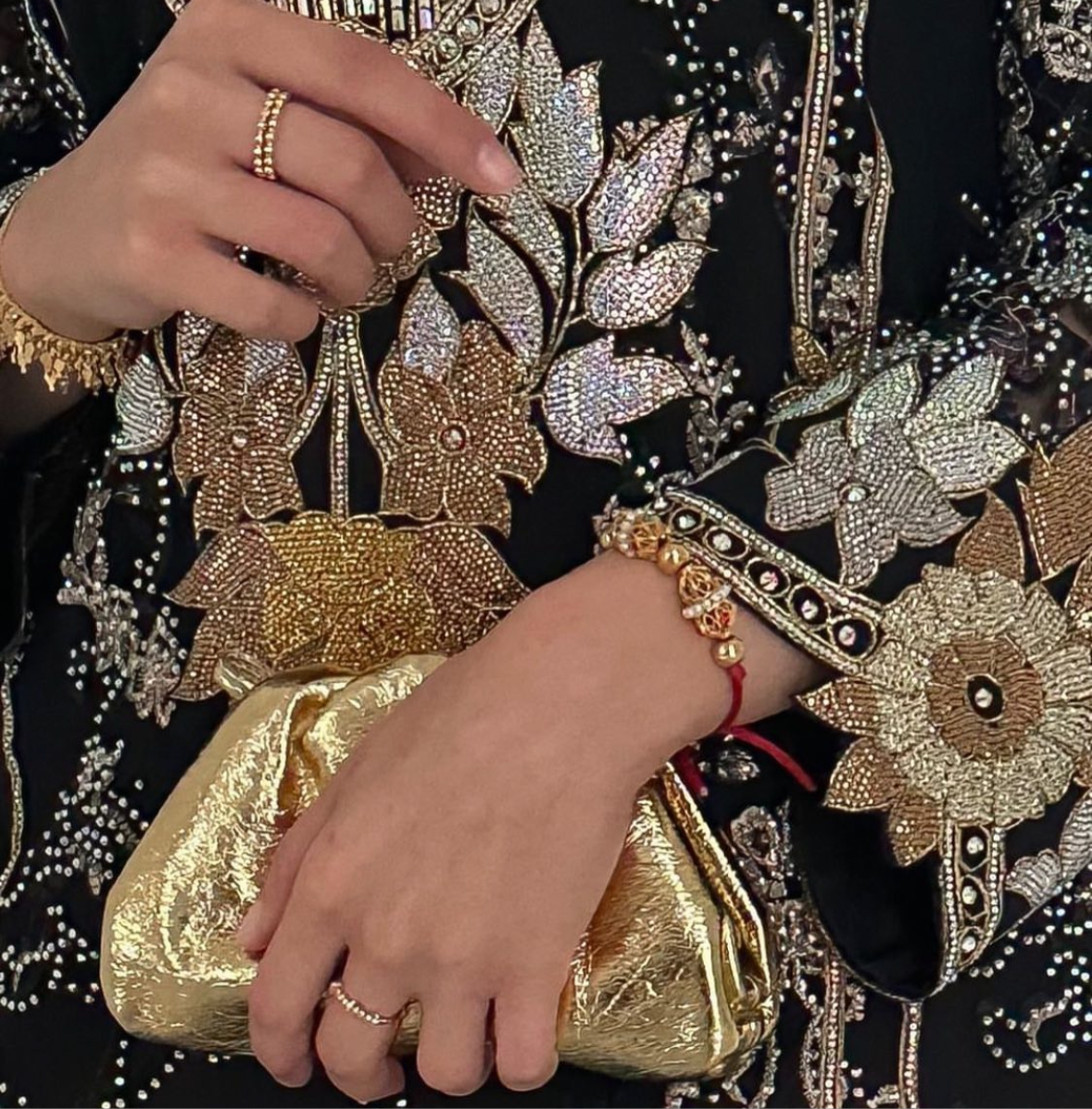 A person's hands holding a small gold-colored micro bag with a short leather strap, featuring a floral pattern on the clothing they are wearing.