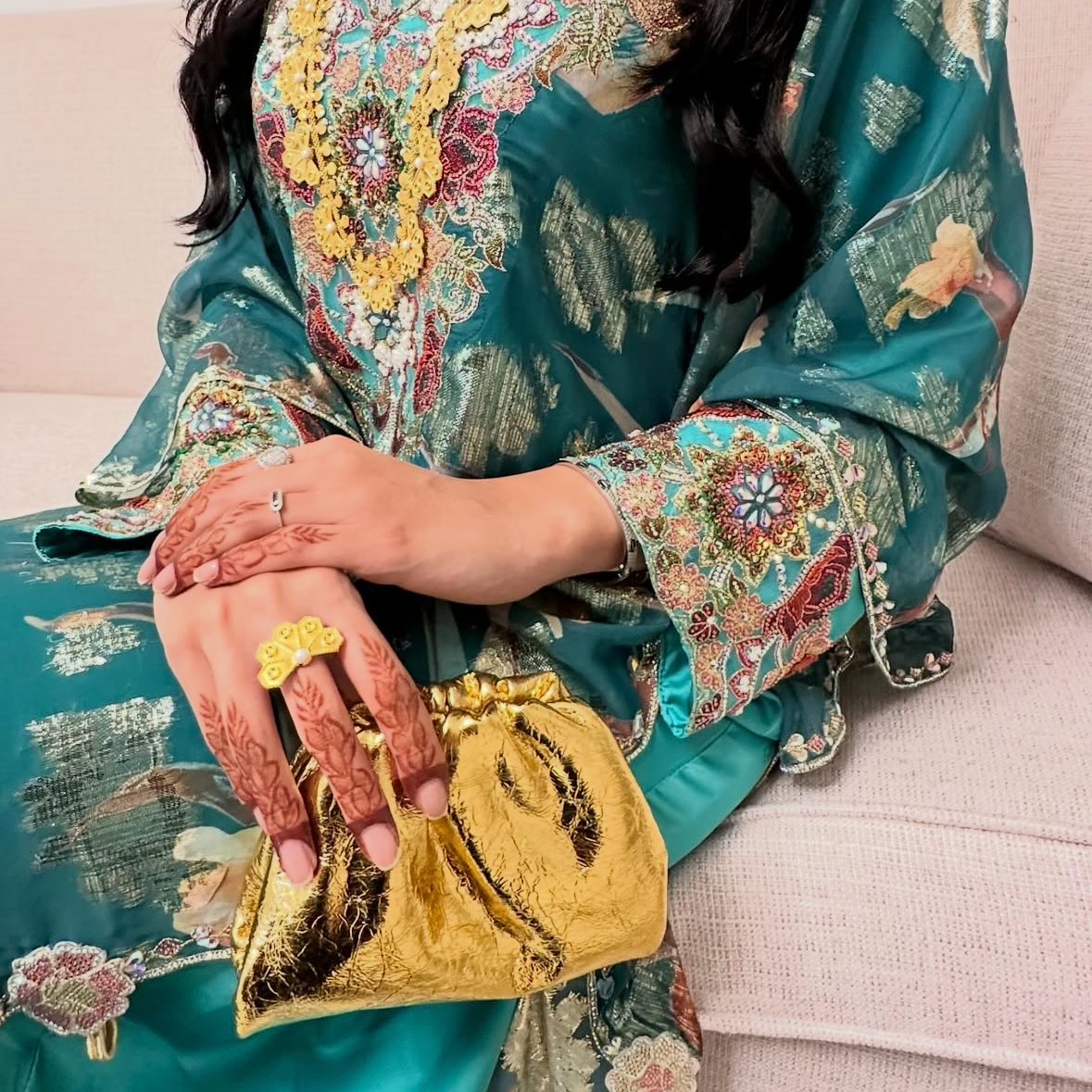 Person wearing a floral dress with gold accents sitting on a couch.