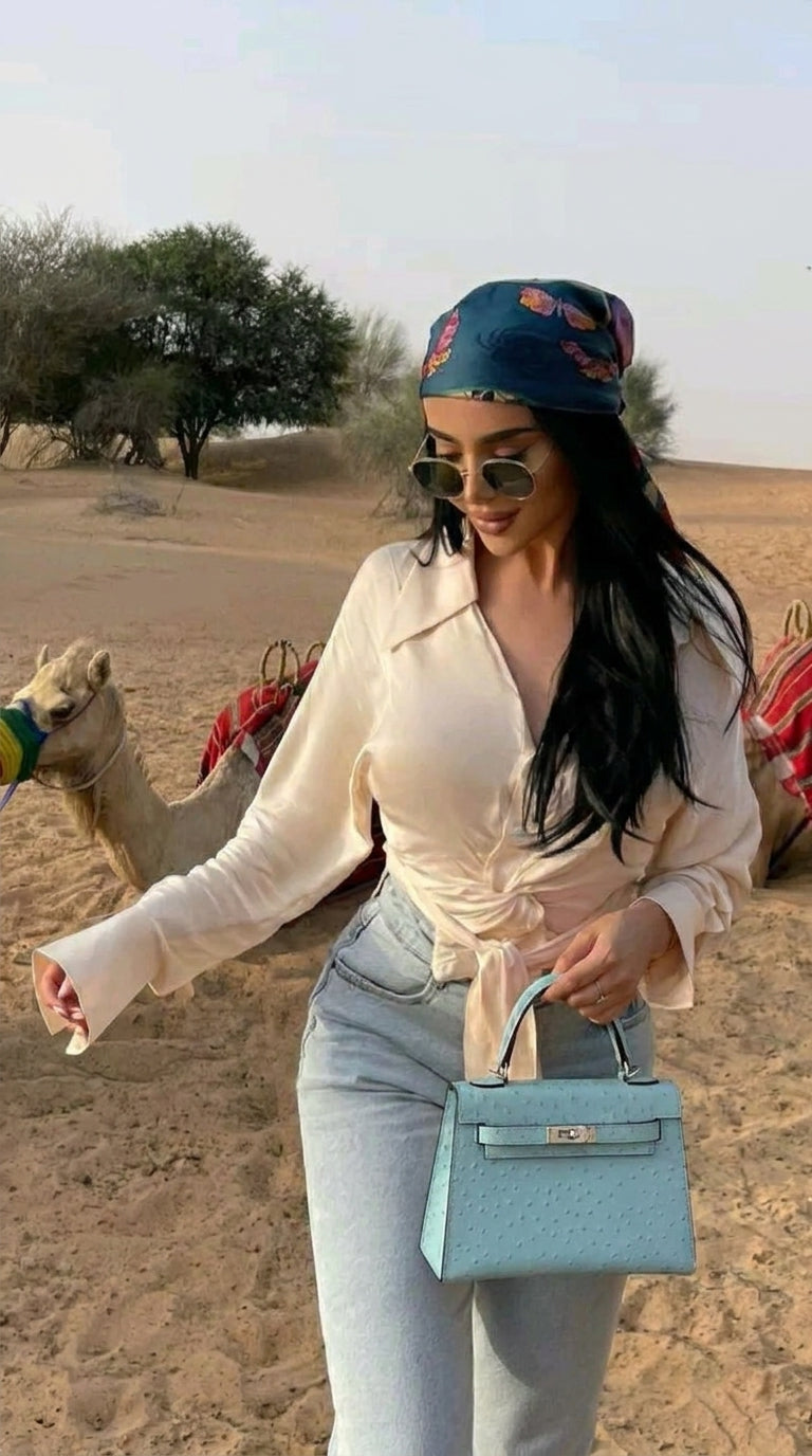Woman in a desert setting with a camel, wearing sunglasses and a headscarf.