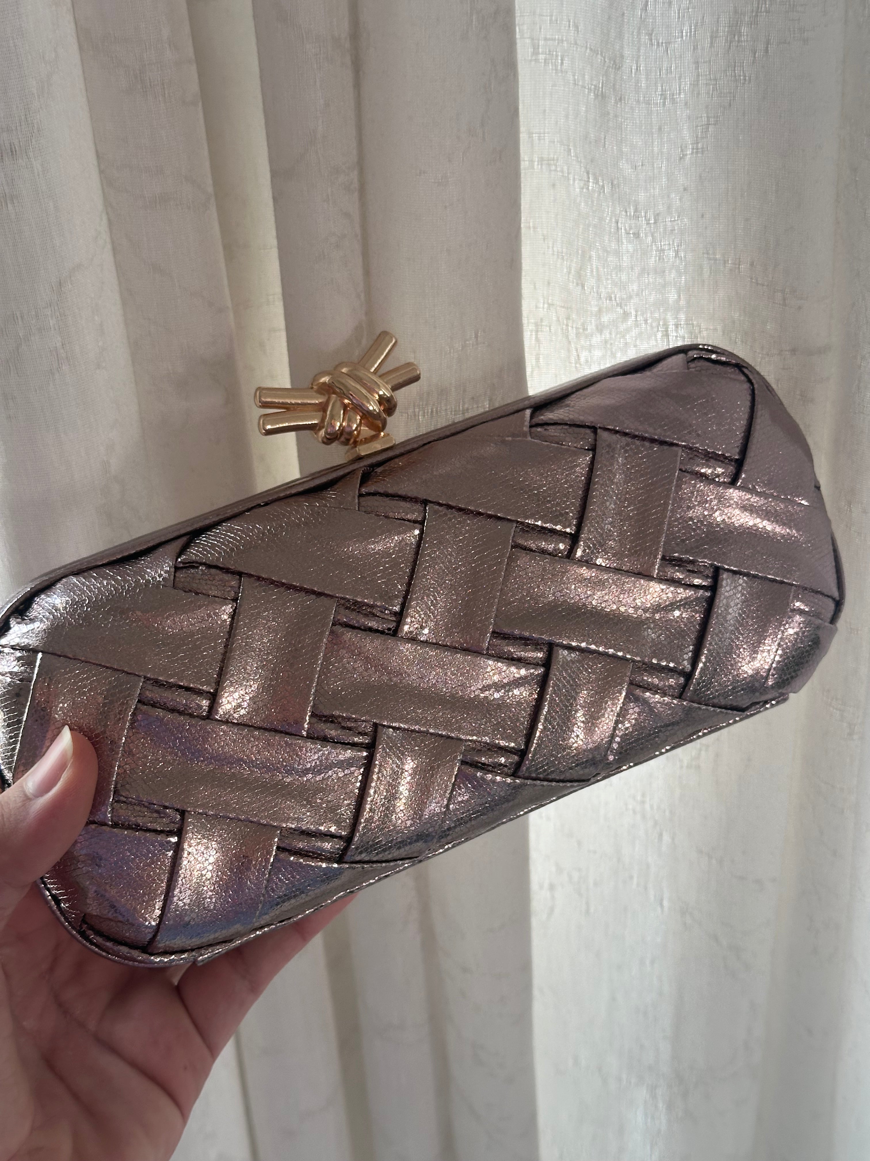 Metallic woven clutch held against a neutral background